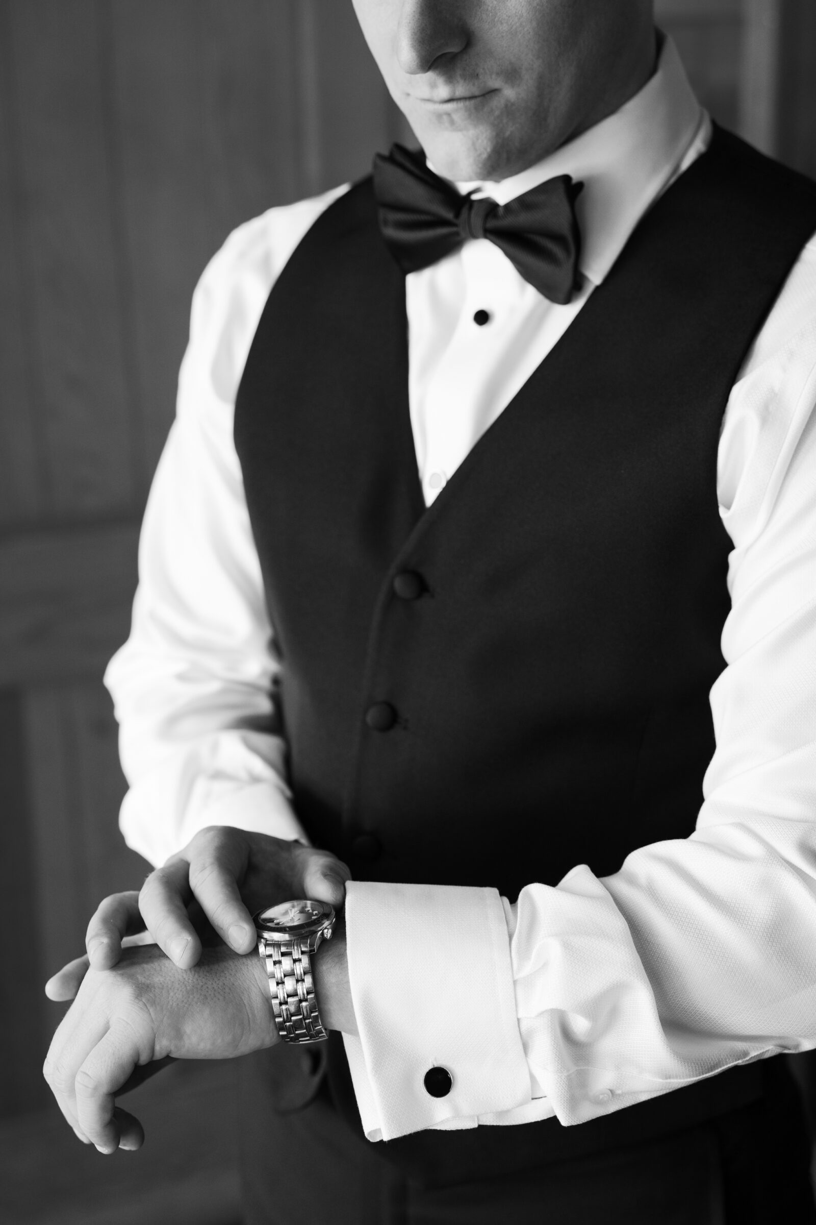 Groom in a classic black vest and bow tie adjusting his watch and cufflinks while getting ready for a September wedding at Middleburg Barn