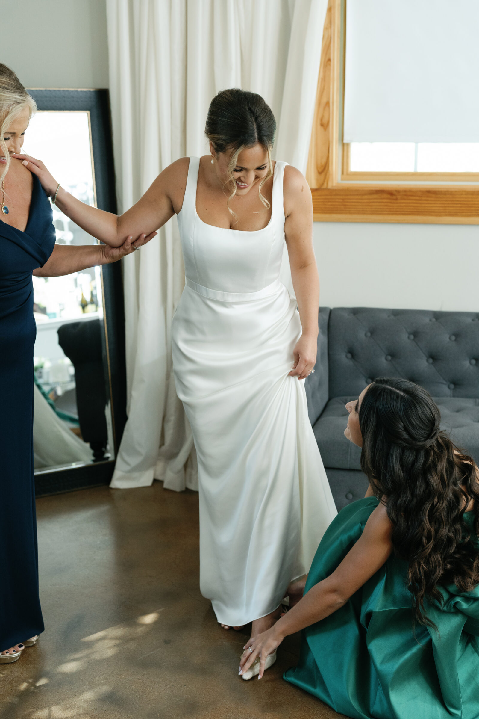 Bride in a satin dress getting ready as a bridesmaid adjusts her shoe during a wedding at Middleburg Barn.