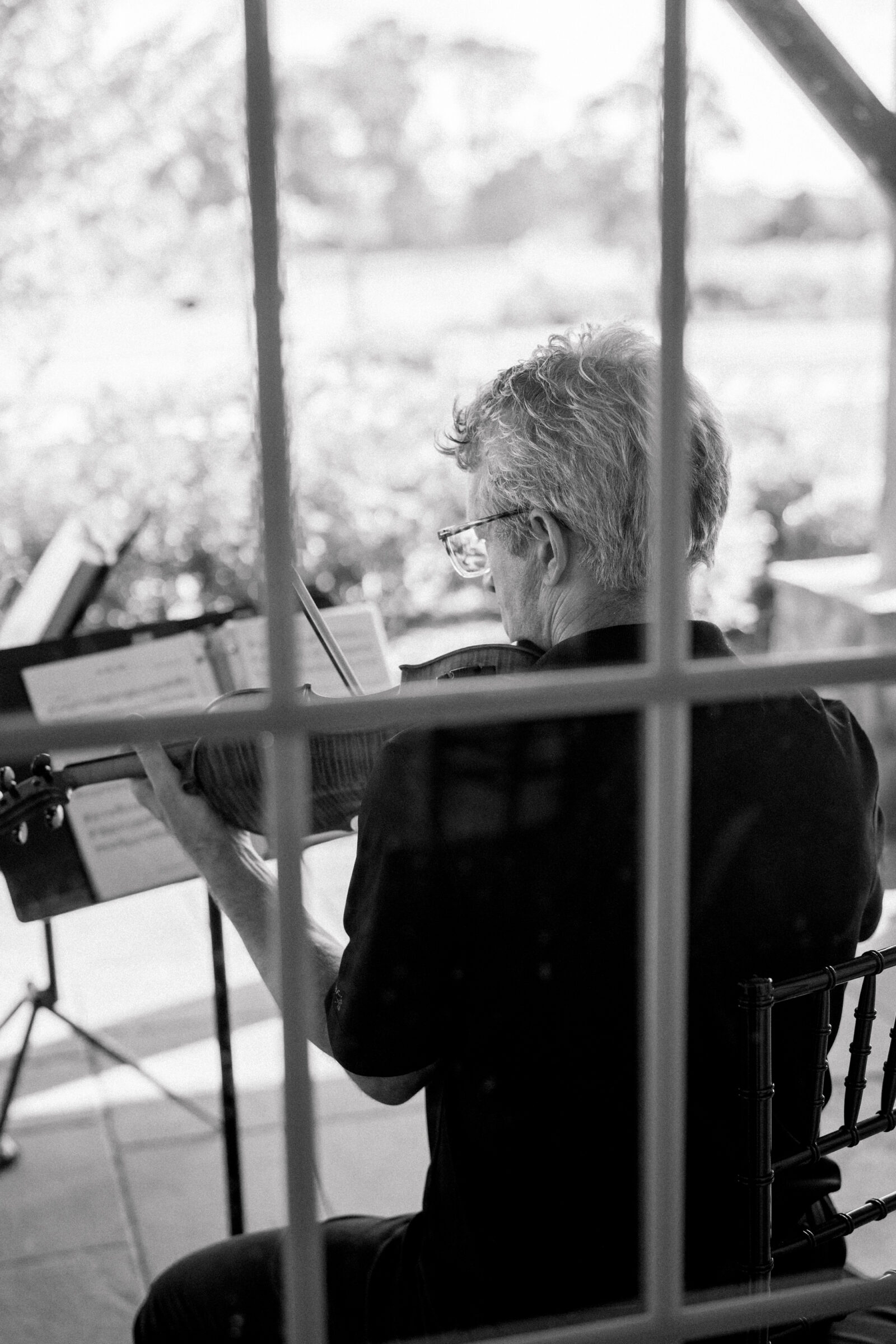Black-and-white image of a violinist seen from behind playing live string music during a wedding ceremony in Middleburg, VA.