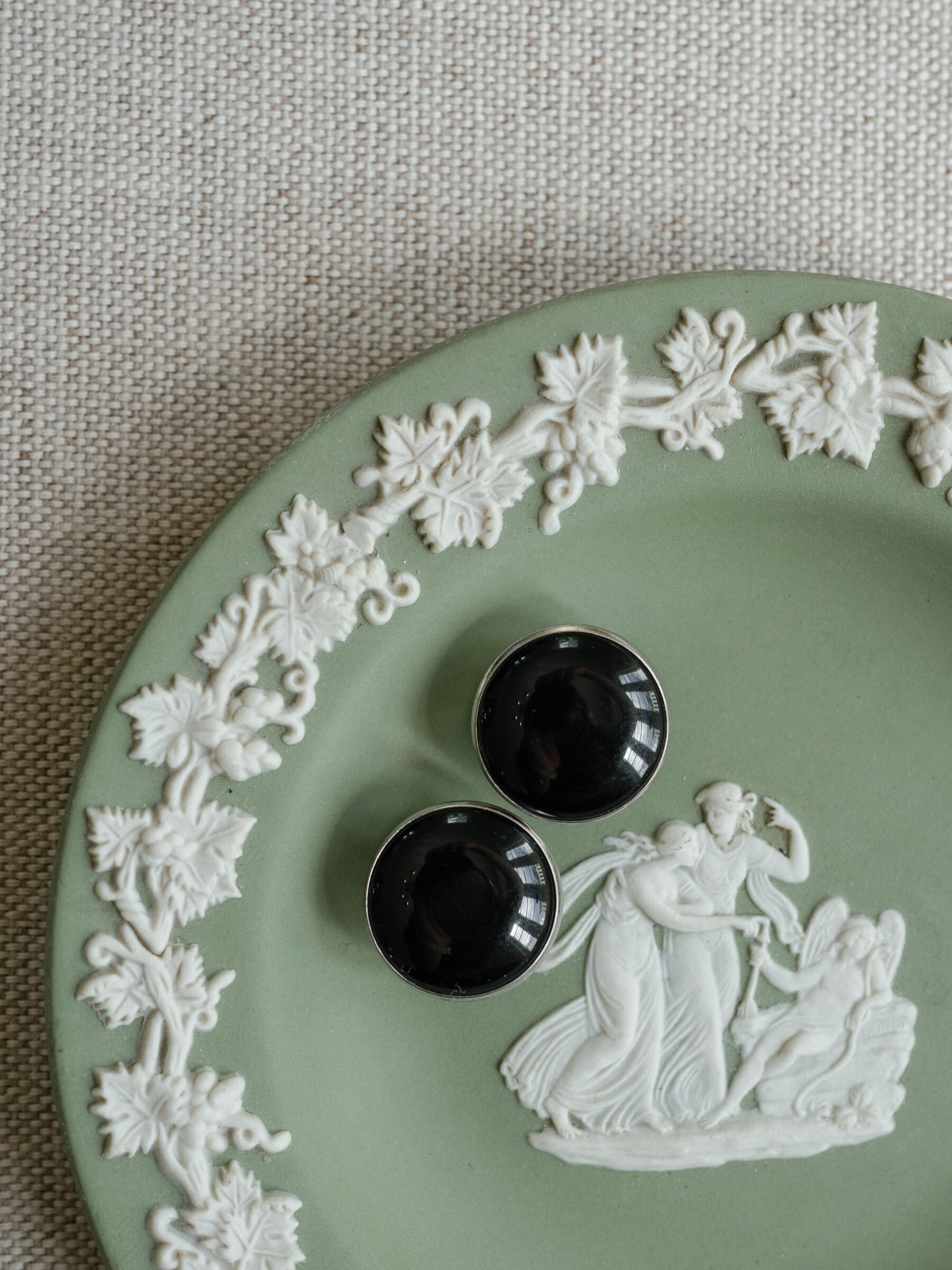 Groom’s black cufflinks styled on a sage green Wedgwood plate with white classical detailing.