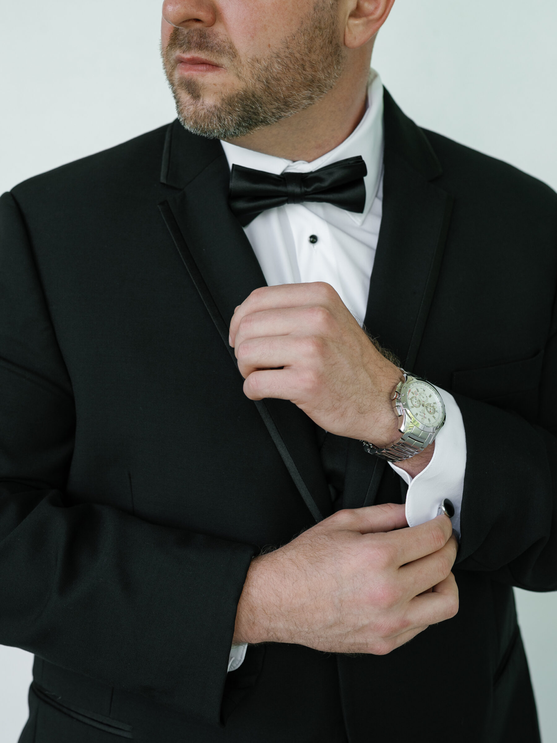 Groom adjusting his cufflinks in a classic black tuxedo with bow tie and silver watch