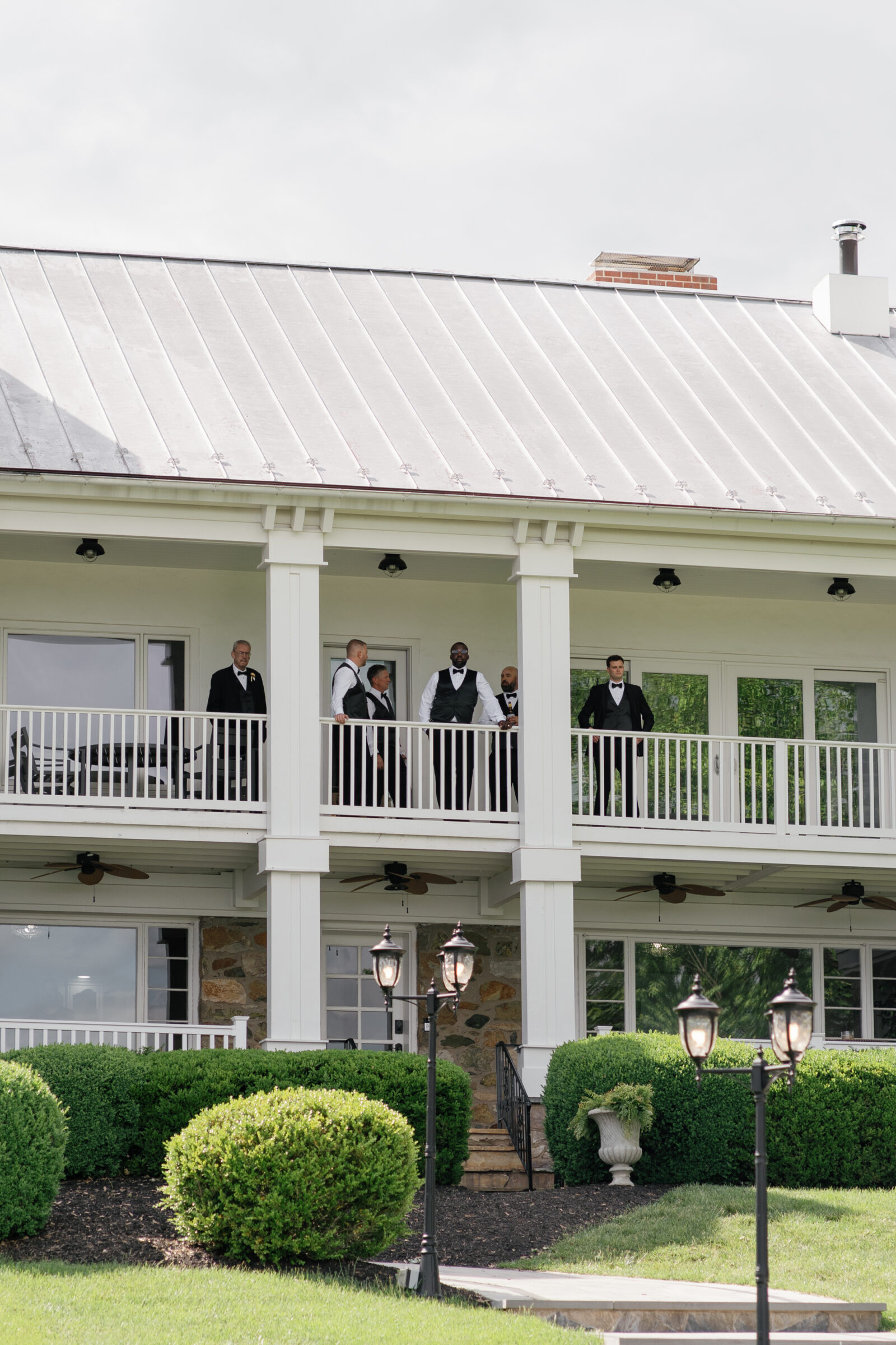 Groomsmen in black tuxedos standing on the balcony of the manor house at The View at Bluemont, a Northern VA wedding venue.