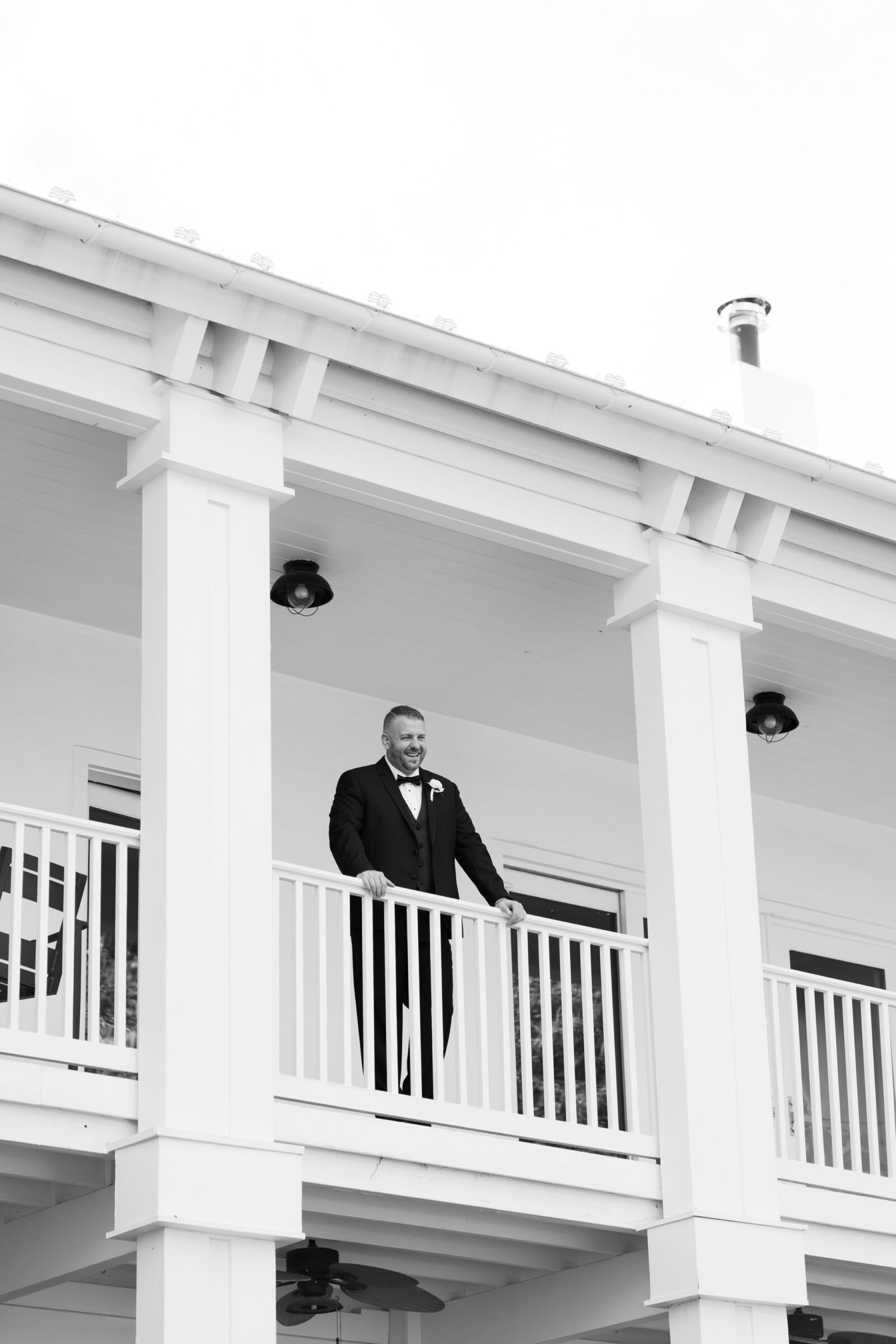 Groom in a classic black tuxedo smiling from the balcony of the manor house at The View at Bluemont wedding in Northern Virginia.