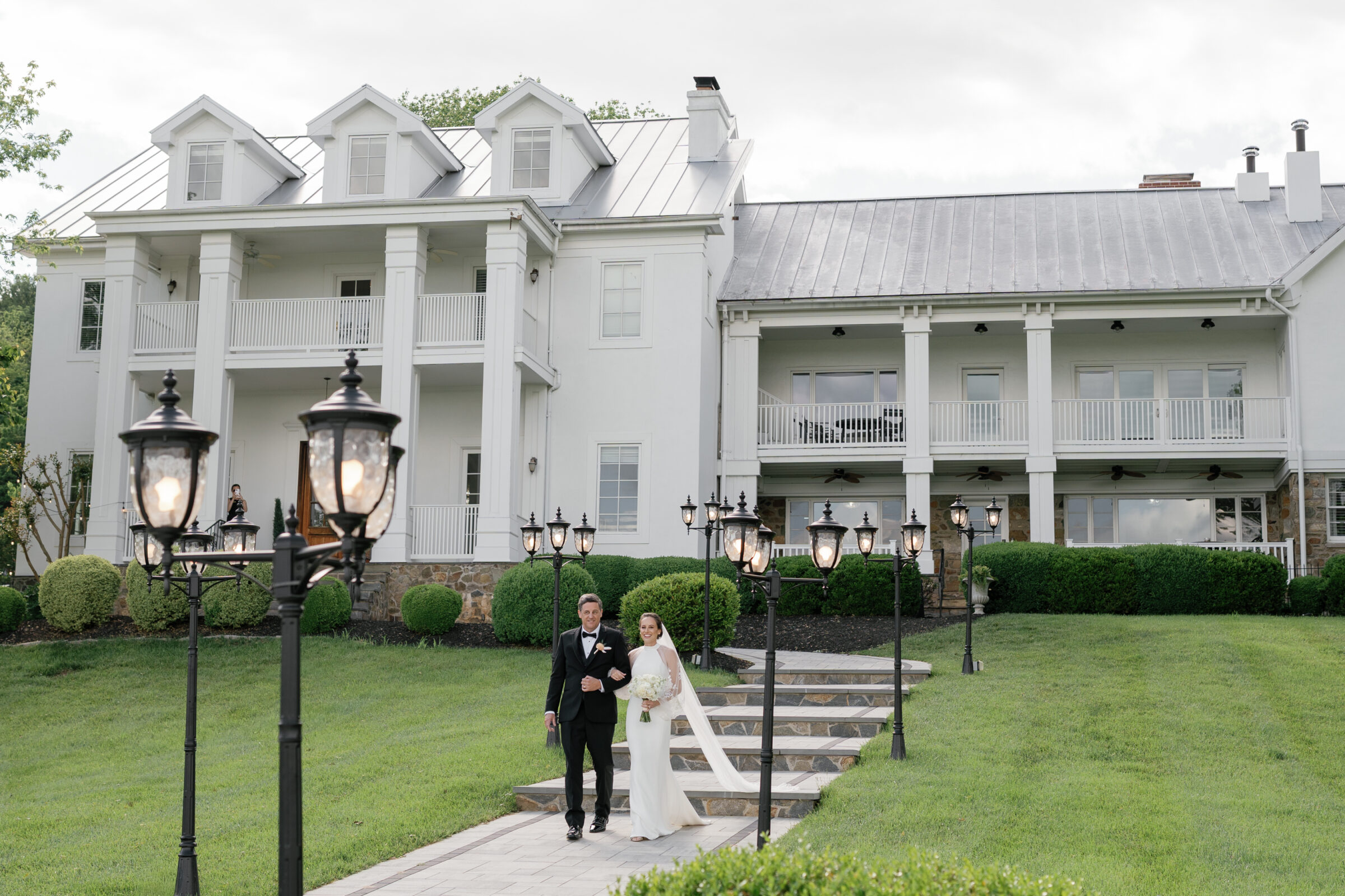 Bride walking down the stone pathway with her father in front of the manor house at The View at Bluemont, an elegant Northern VA wedding venue.