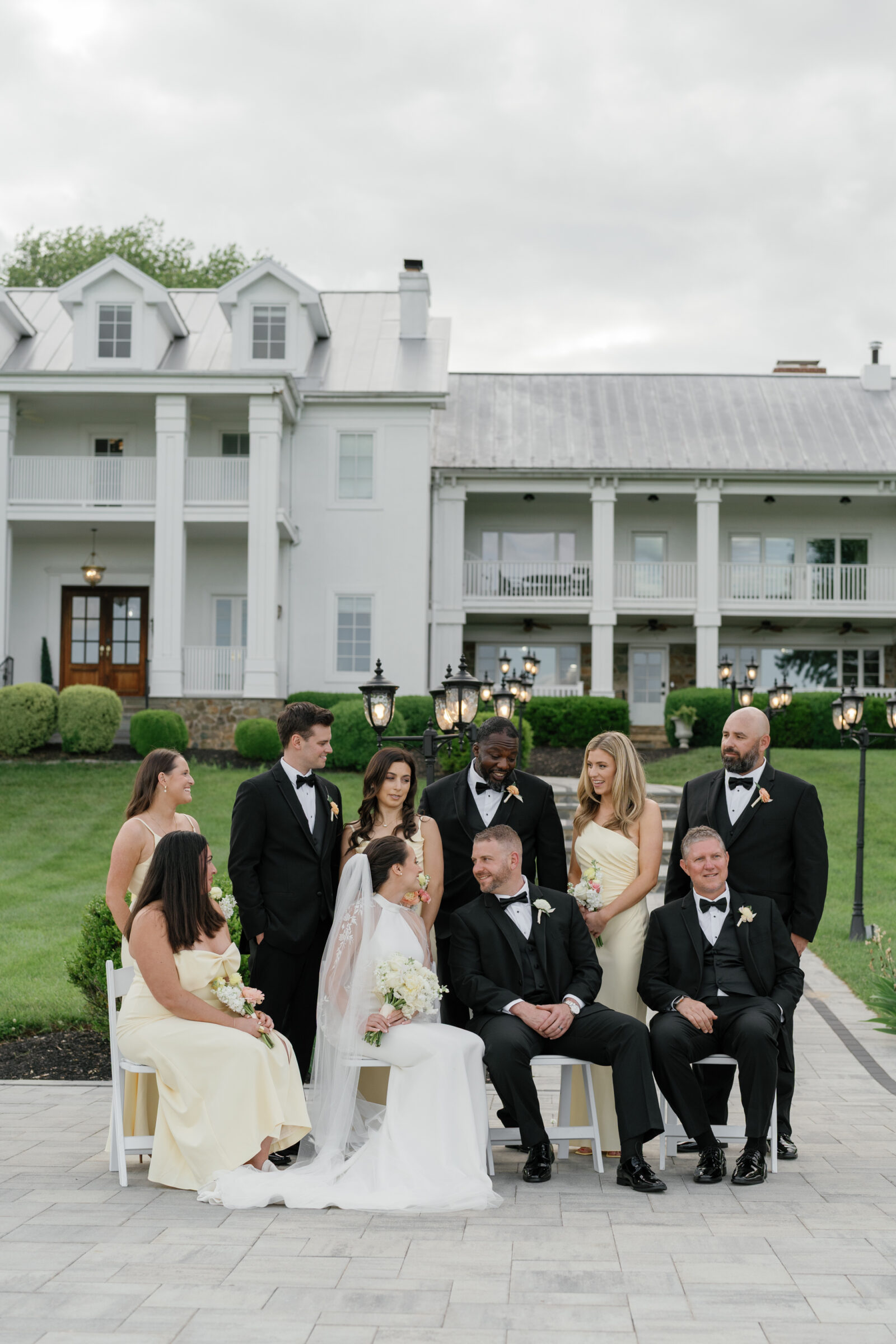 The bride and groom share a joyful moment with their wedding party in front of the elegant white manor house at The View at Bluemont, a scenic Northern Virginia wedding venue.