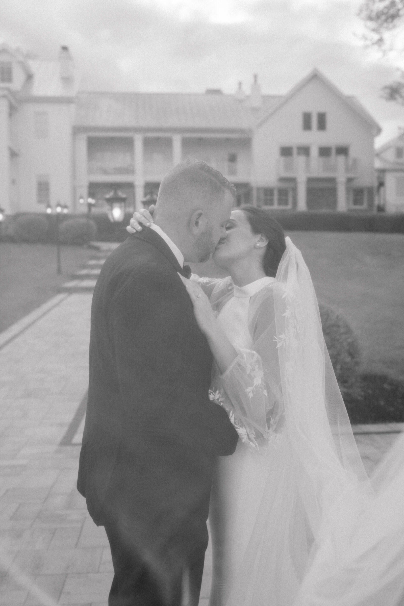Black and white wedding photo of a bride and groom sharing a kiss outside The View at Bluemont, a Northern Virginia wedding venue with a grand white manor backdrop.