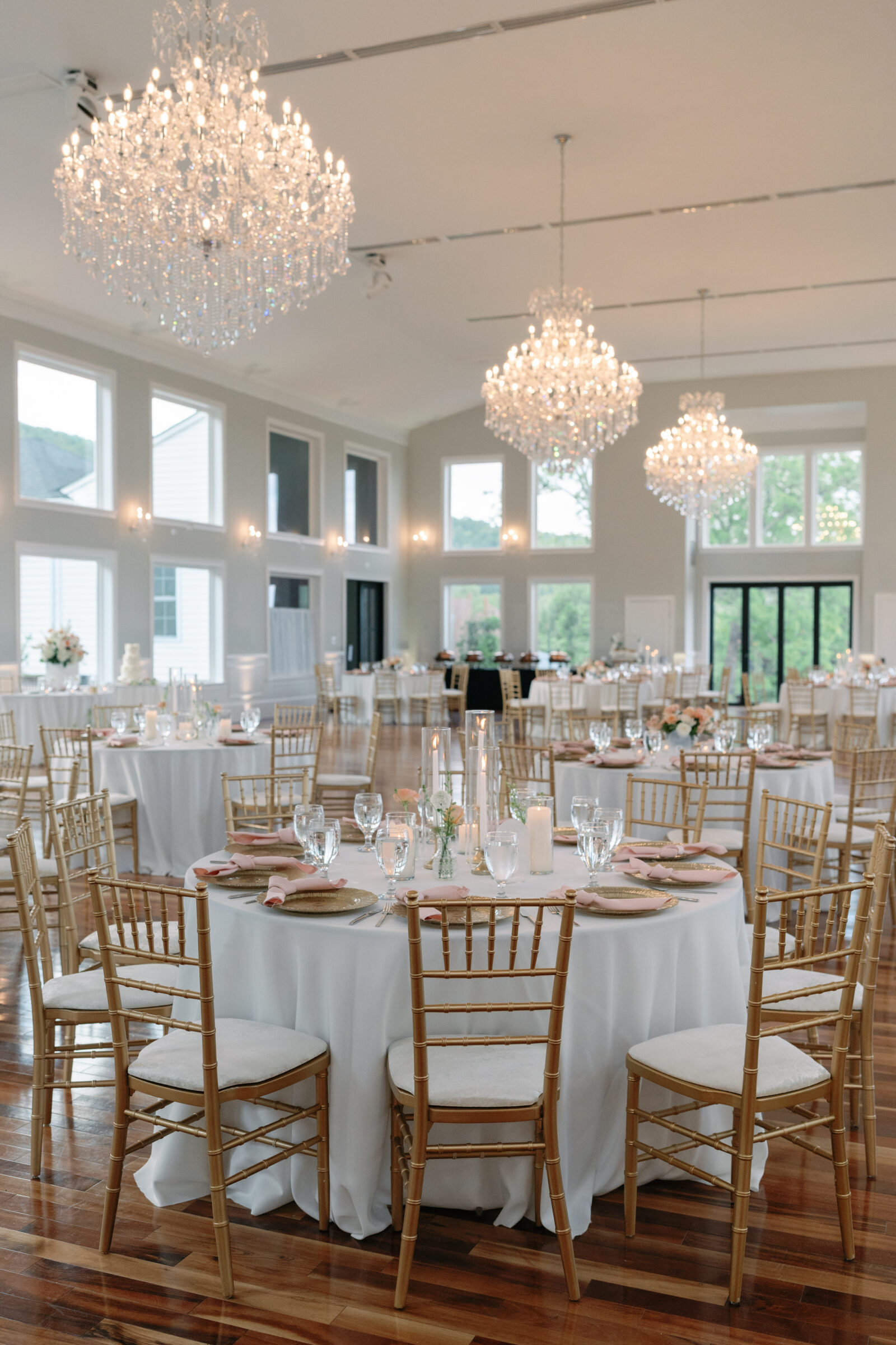 Elegant wedding reception setup at The View at Bluemont in Northern Virginia, featuring gold chiavari chairs, white linens, blush accents, and grand crystal chandeliers.