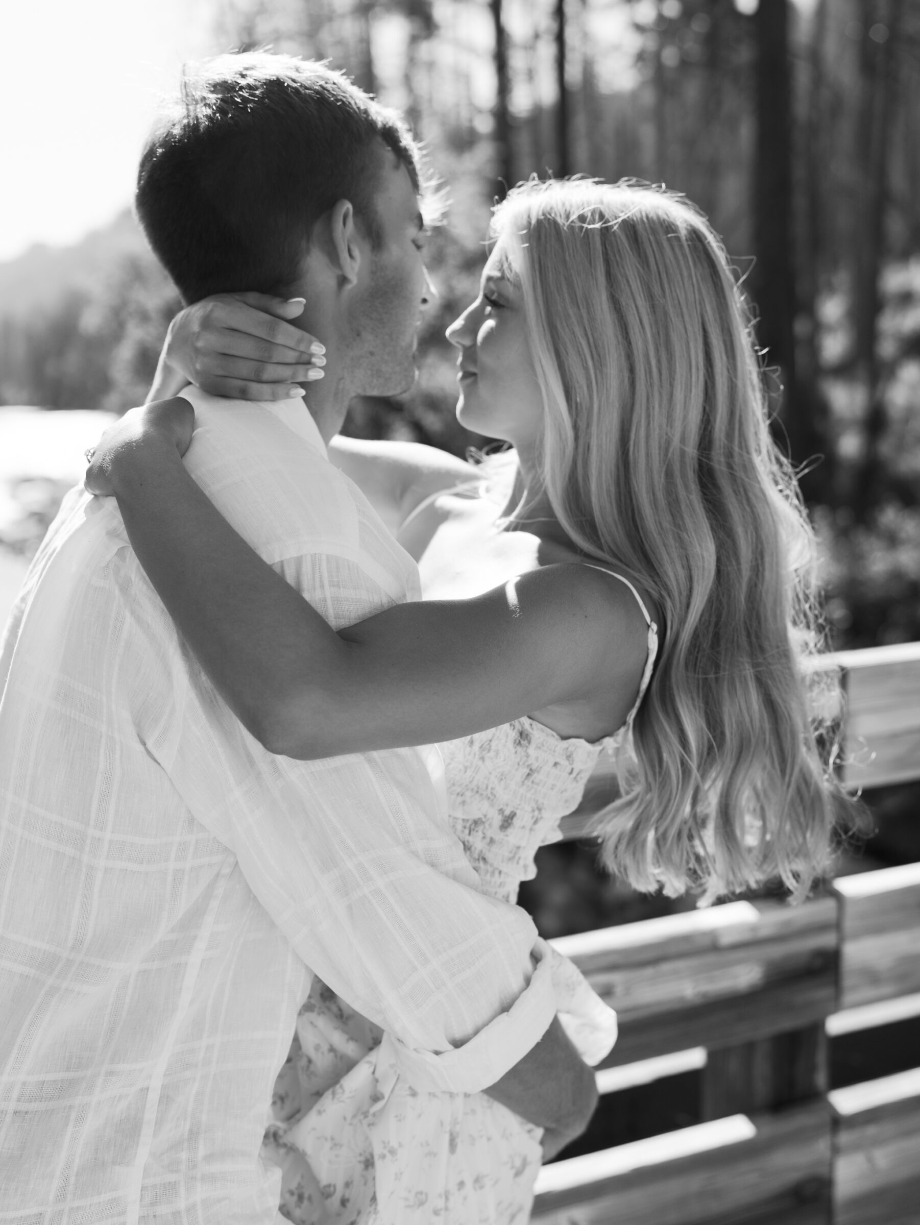 Black and white photo of a couple embracing closely on a wooden bridge during their Umpqua River engagement session, with soft light and forest in the background.