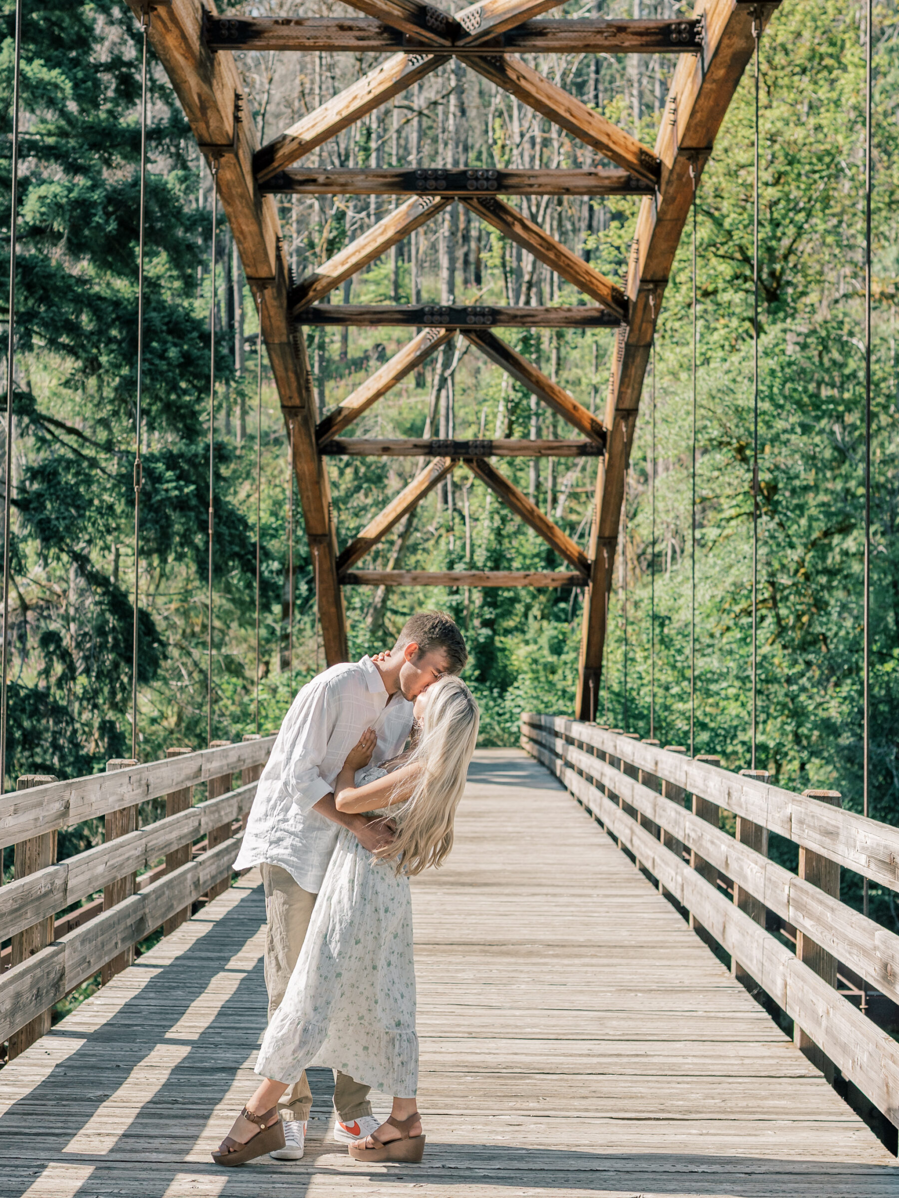 Couple sharing a romantic kiss on a wooden suspension bridge during their Umpqua River engagement session, surrounded by forest in Southern Oregon.