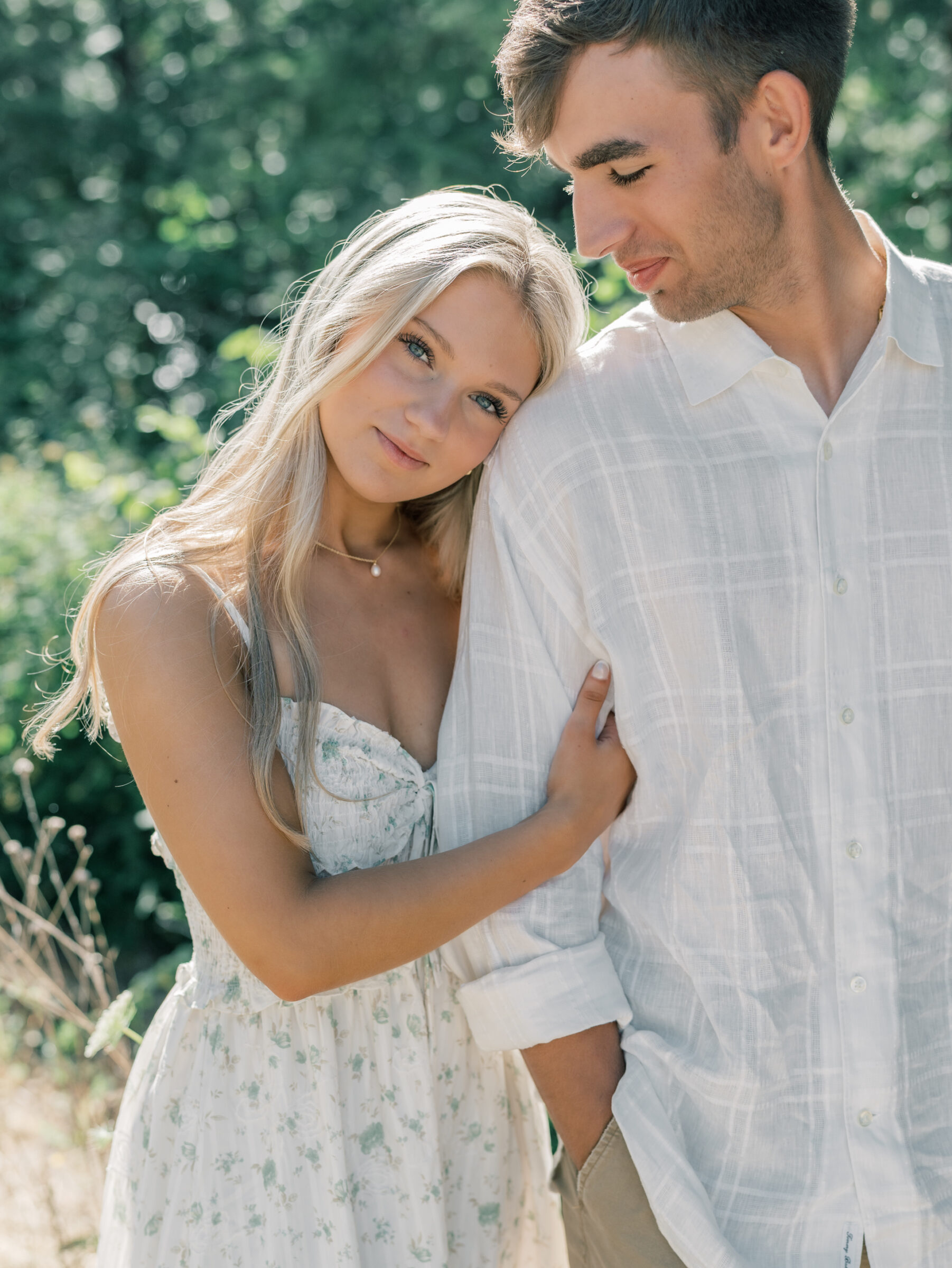 Bride-to-be resting her head on her fiancé’s shoulder during their Umpqua River engagement session, with soft sunlight and greenery in the background.