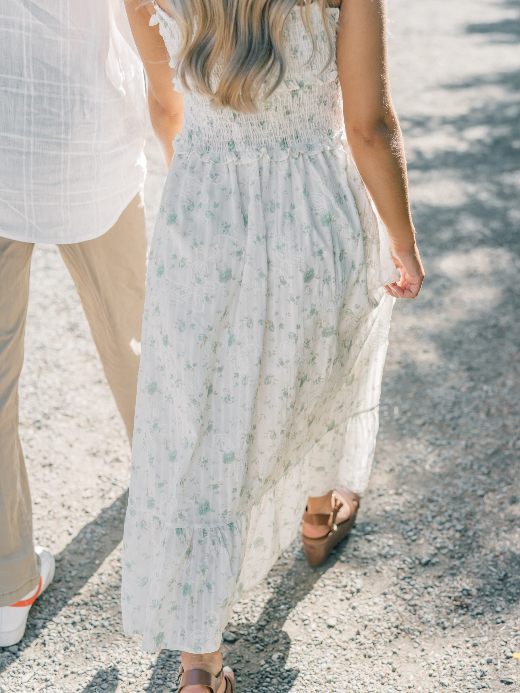 Close-up of couple walking hand in hand during their Oregon engagement session, with the bride-to-be holding her floral dress along a gravel path.