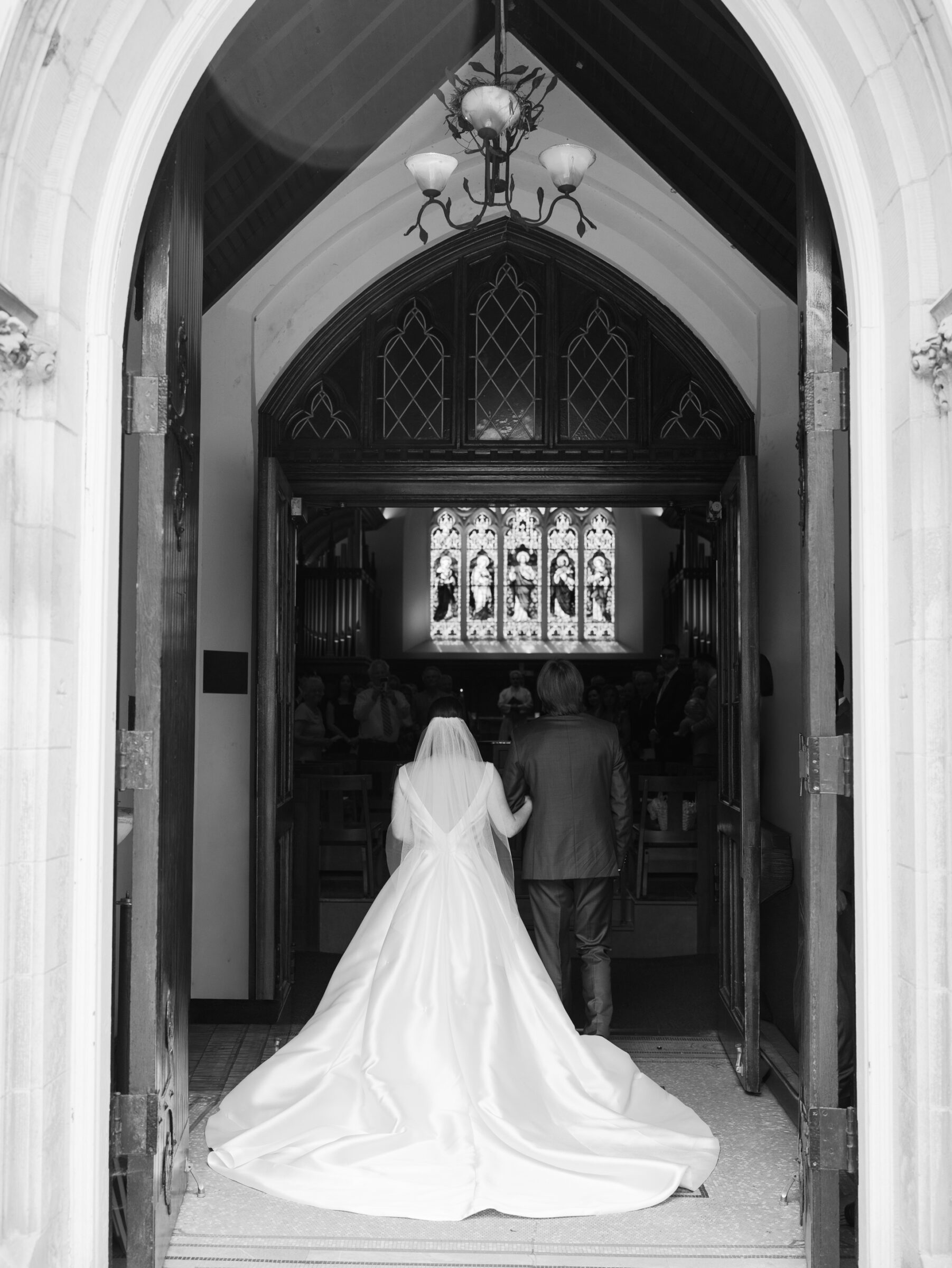 Bride in a long satin gown and veil walking into Dahlgren Chapel at Georgetown University for a Catholic wedding ceremony in Washington DC.