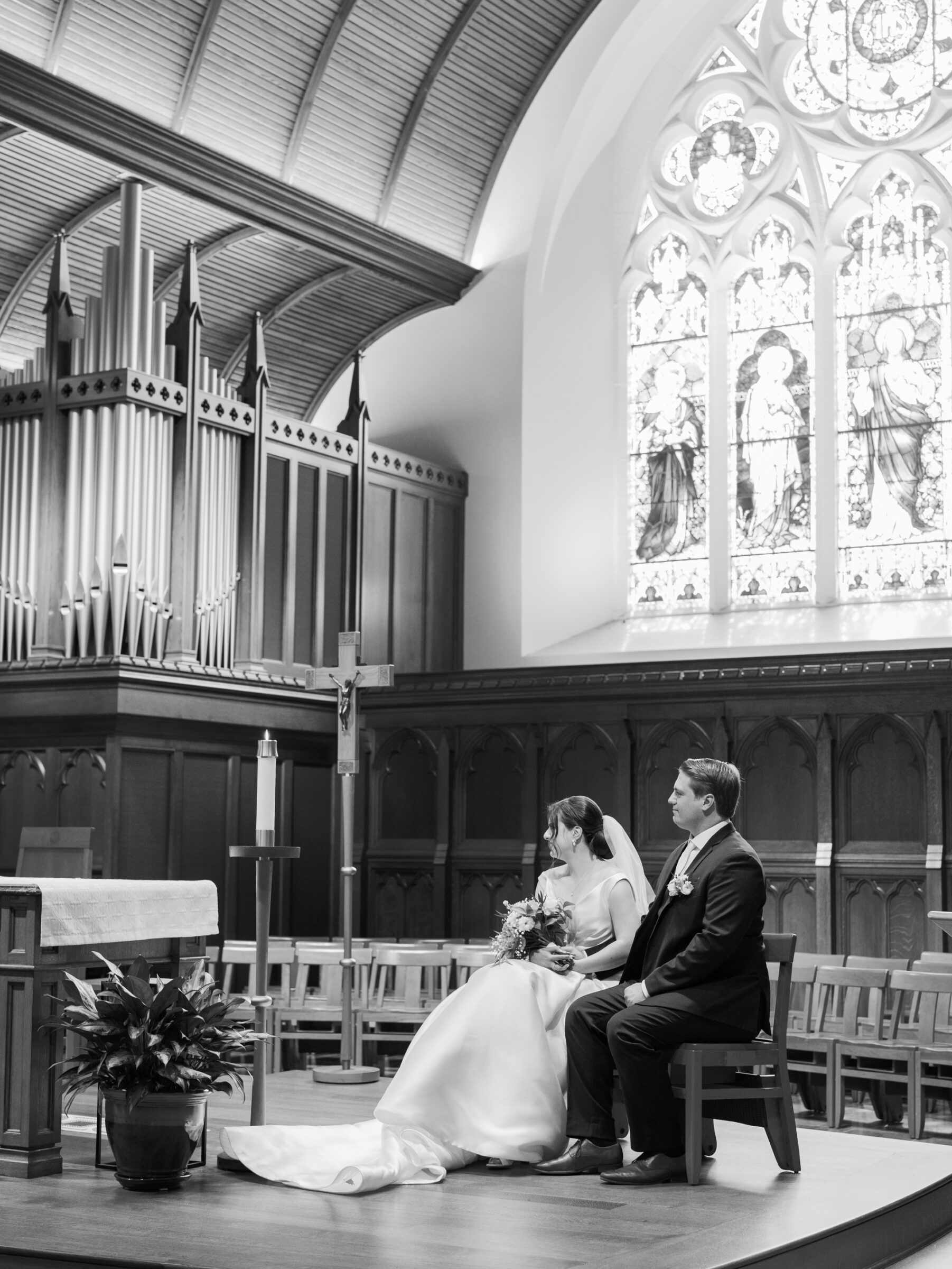 Bride and groom seated at the altar of Dahlgren Chapel at Georgetown University during a Catholic wedding ceremony with stained glass and pipe organ backdrop.