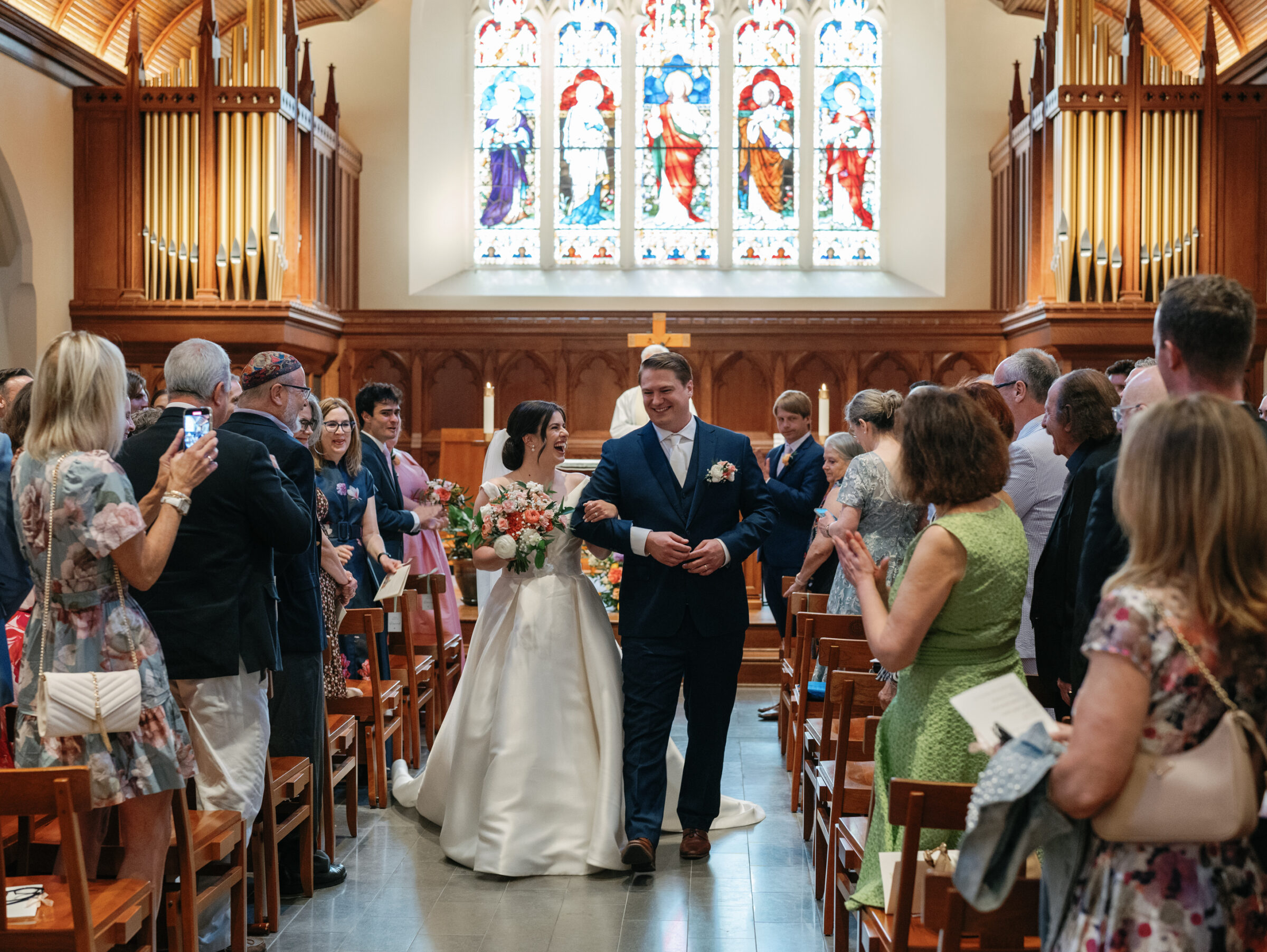 Bride and groom walking down the aisle at Dahlgren Chapel at Georgetown University after their Catholic wedding ceremony, surrounded by guests and stained glass.