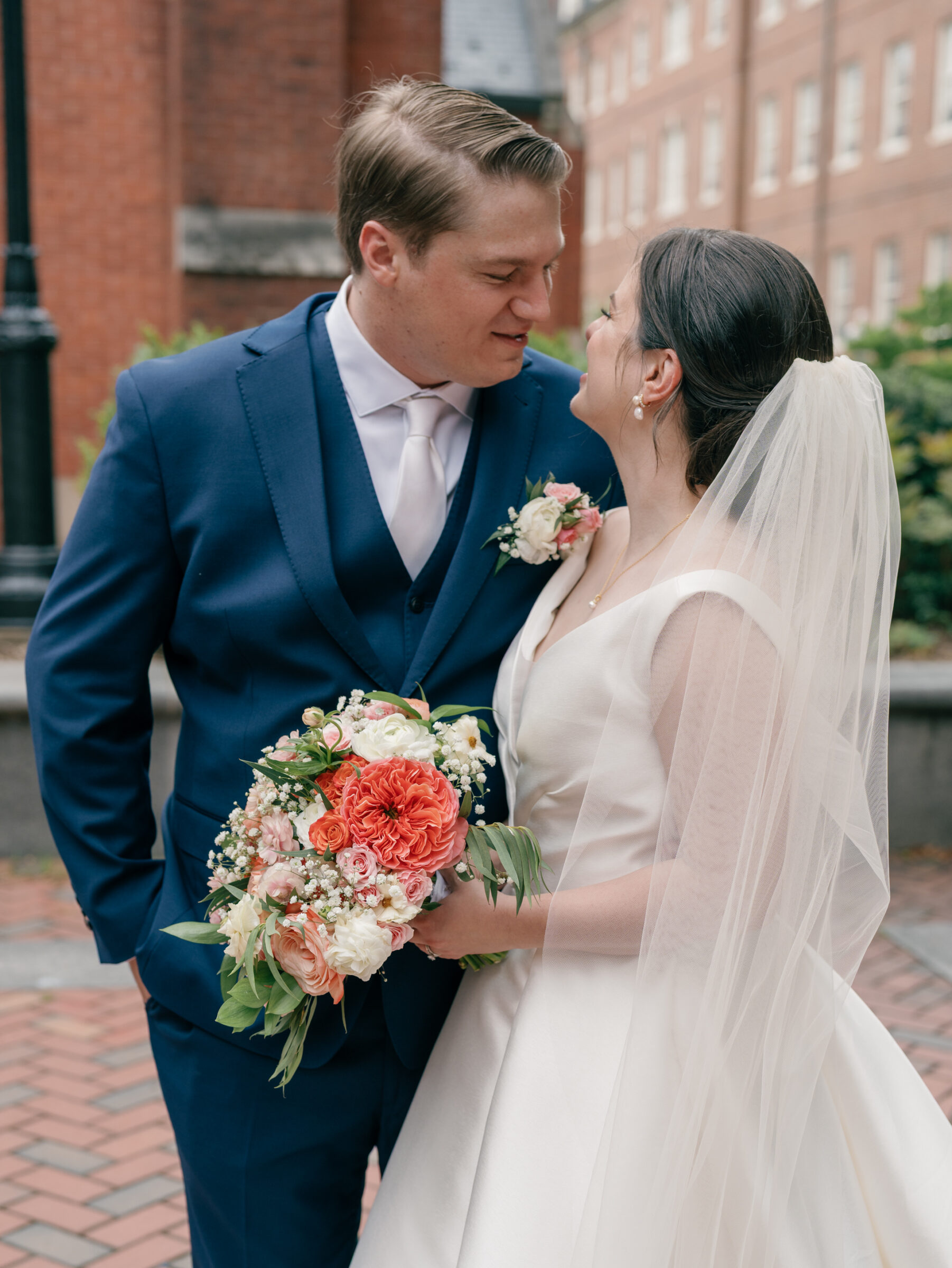 Bride and groom sharing a joyful moment outside Georgetown University after their Catholic wedding at Dahlgren Chapel, holding a colorful pink and coral bouquet.