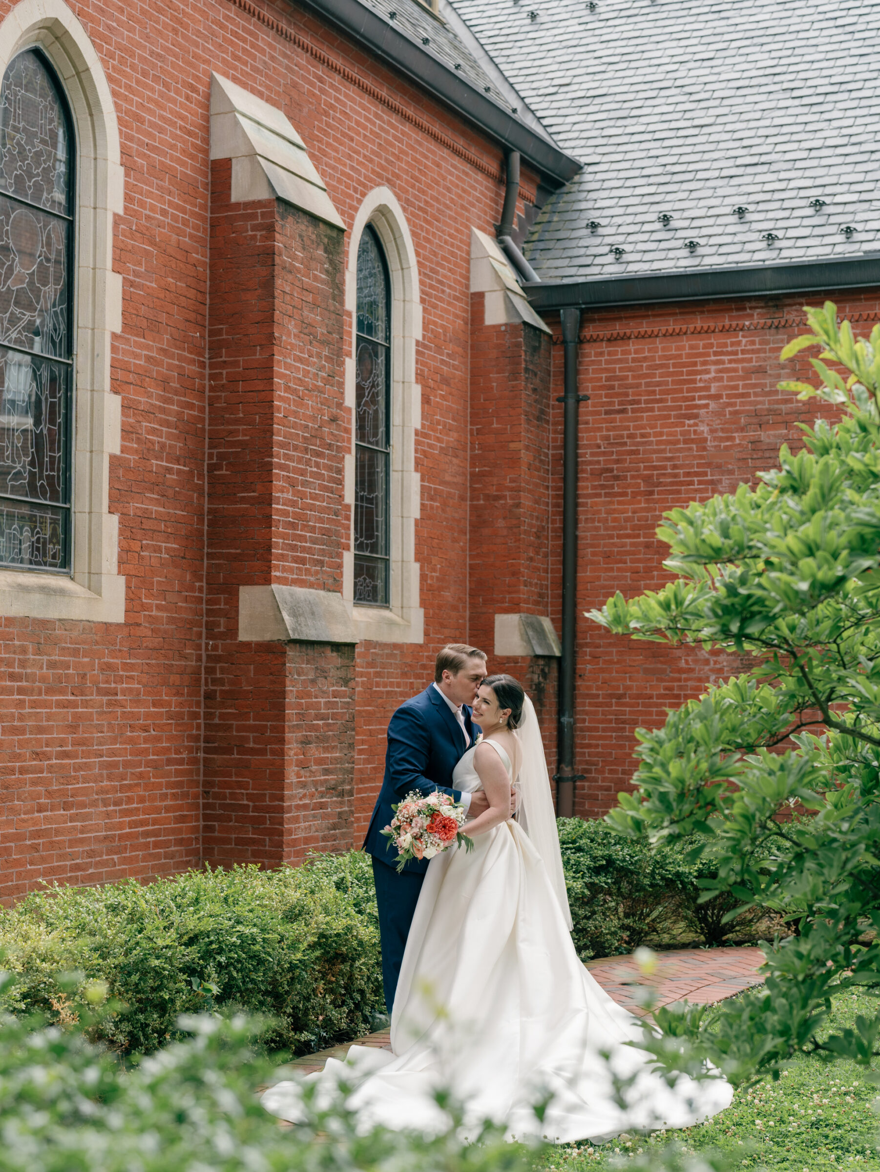 Bride and groom sharing a romantic portrait outside the brick exterior of Dahlgren Chapel at Georgetown University after their Catholic DC wedding ceremony.