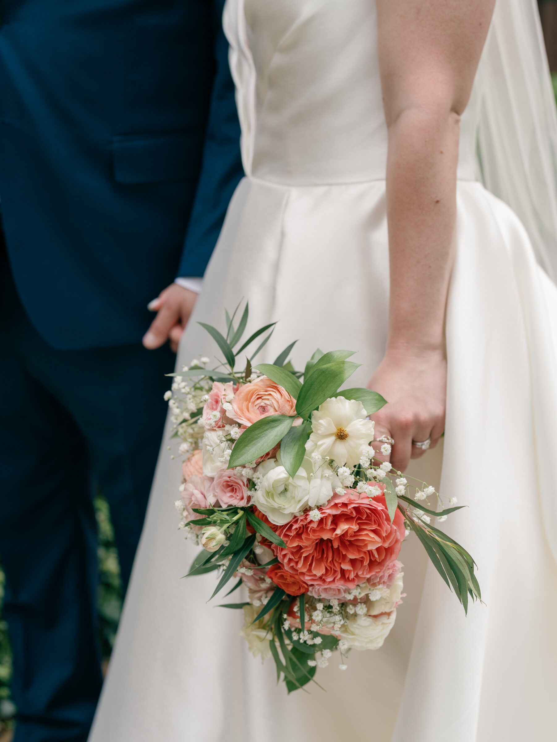 Close-up of the bride holding a pink and coral bouquet with greenery during portraits at Georgetown University after a Catholic wedding ceremony at Dahlgren Chapel.