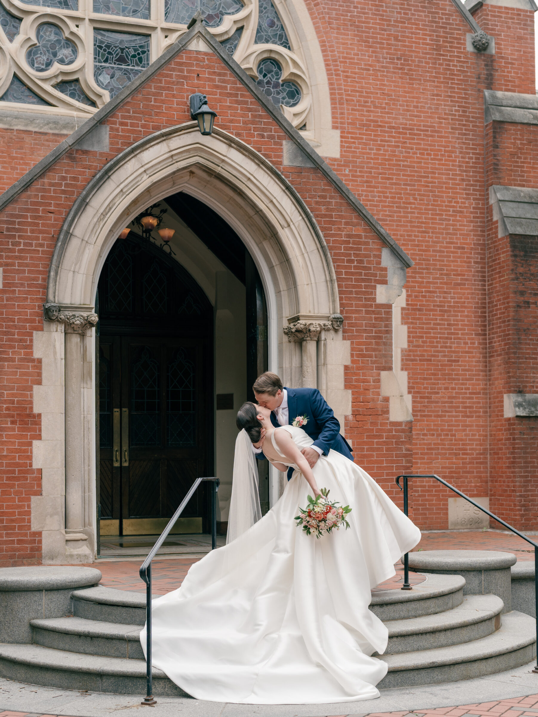 Bride and groom sharing a dip kiss outside the arched doorway of Dahlgren Chapel at Georgetown University after their DC Catholic wedding ceremony.