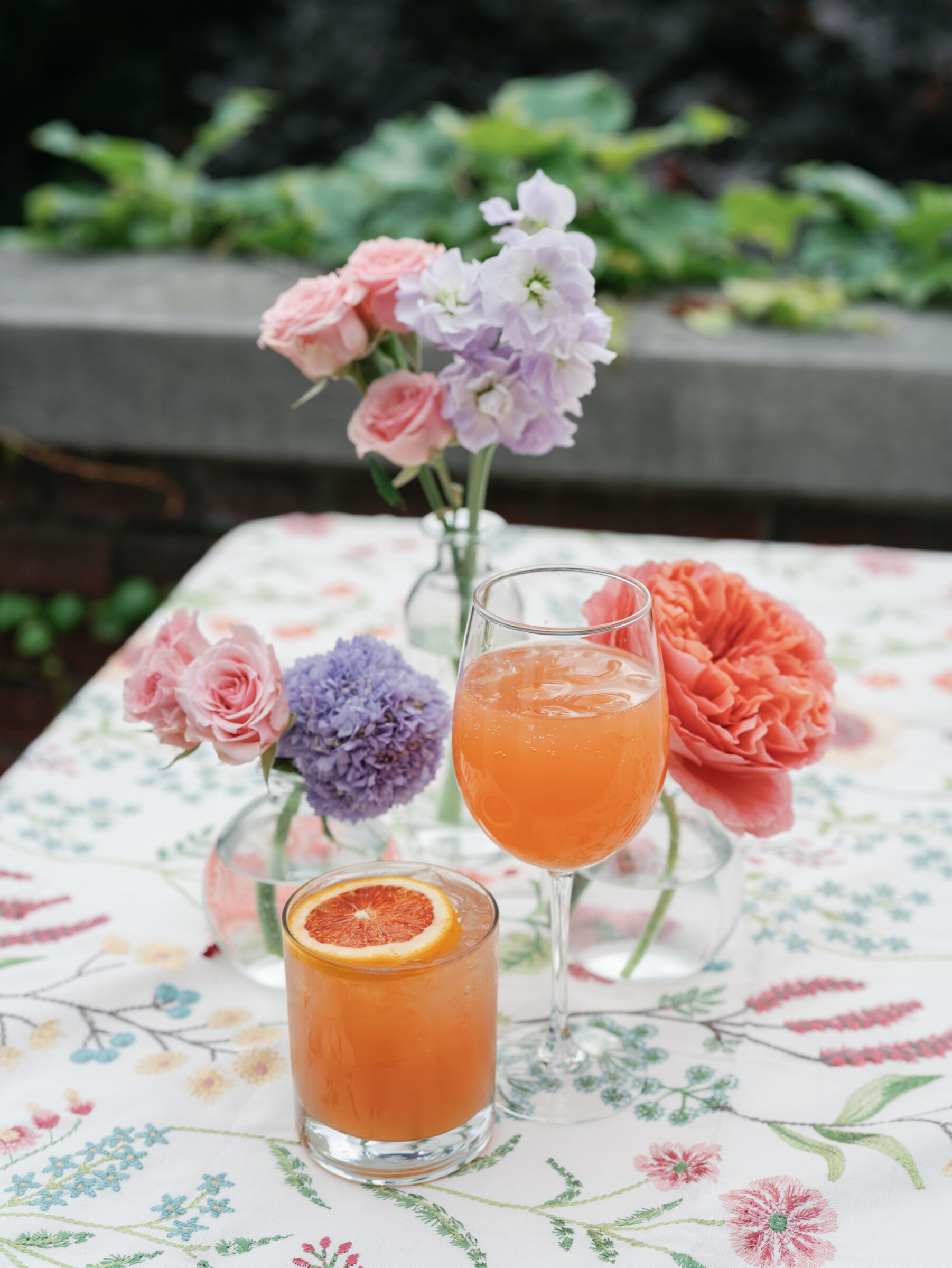 Colorful cocktails with citrus garnish and pastel floral centerpieces on a patterned tablecloth during cocktail hour at a Woodrow Wilson House Wedding in Washington DC.