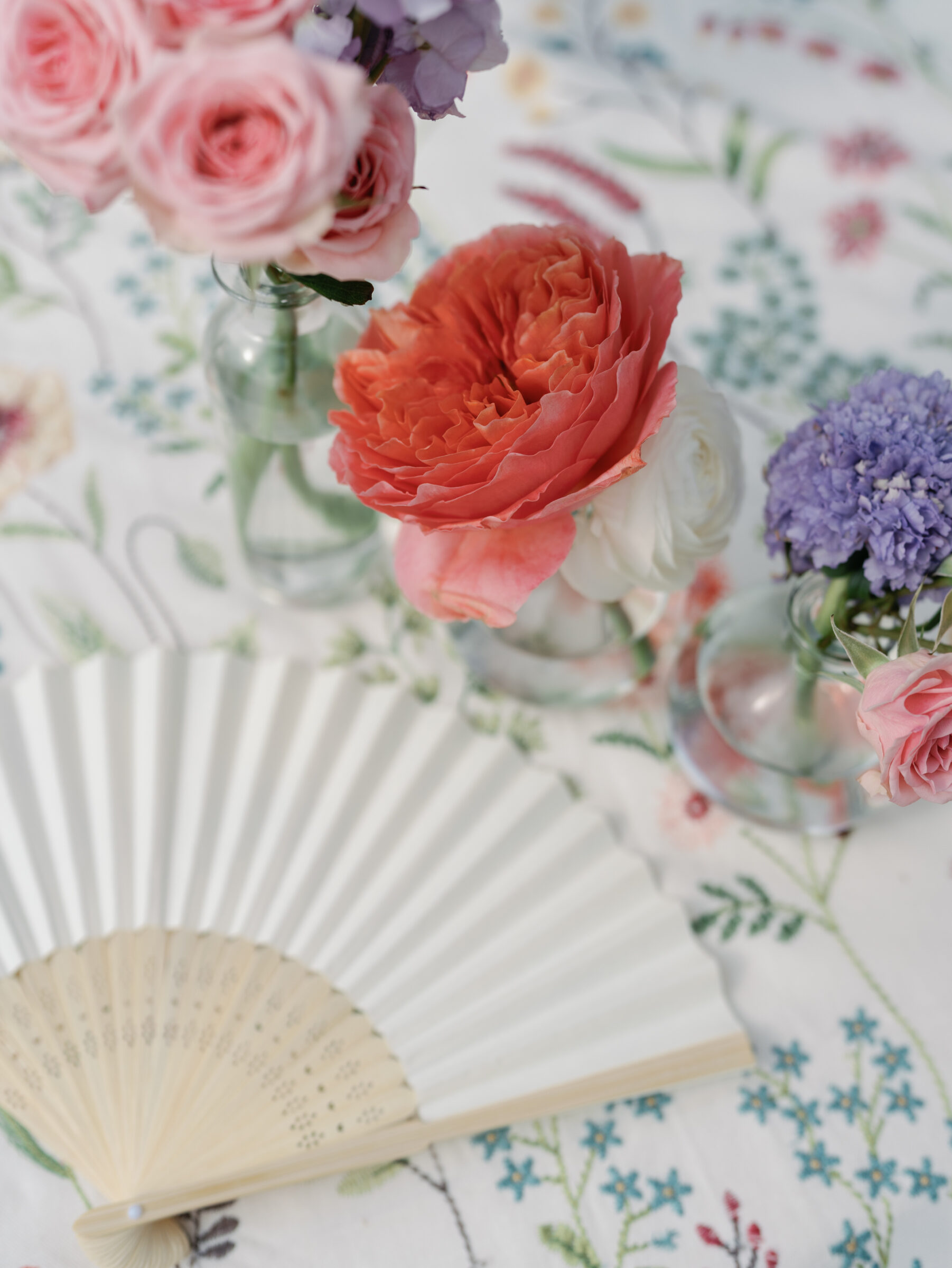 Colorful pink, coral, and purple floral centerpieces with a handheld fan on patterned linens during cocktail hour at a Woodrow Wilson House Wedding in Washington DC.