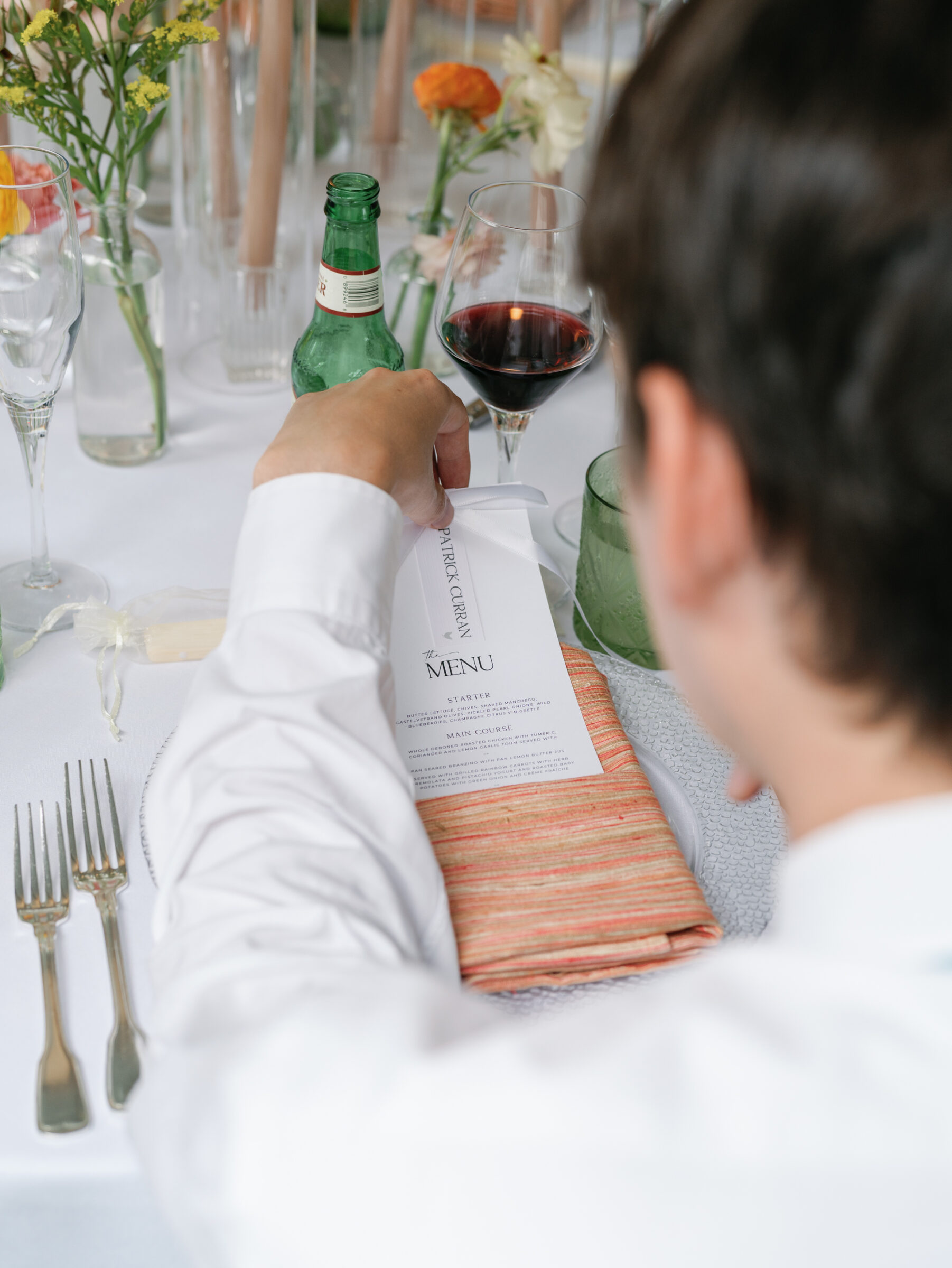 Wedding guest reading the dinner menu at a beautifully set reception table with wine and floral centerpieces during a Woodrow Wilson House Wedding in Washington DC.