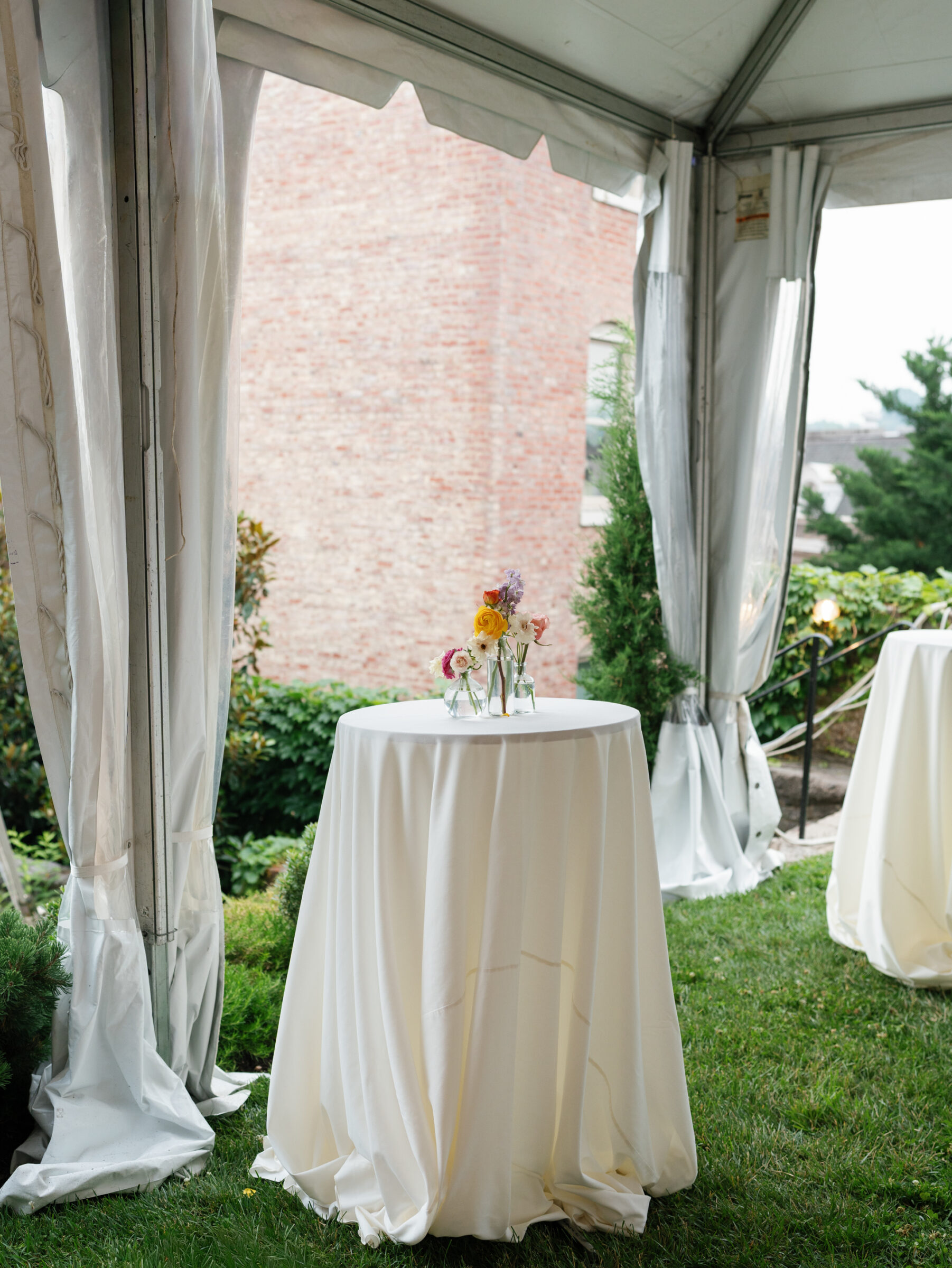 Cocktail table with white linens and small floral arrangements set inside the reception tent on the lawn at a Woodrow Wilson House Wedding in Washington DC.