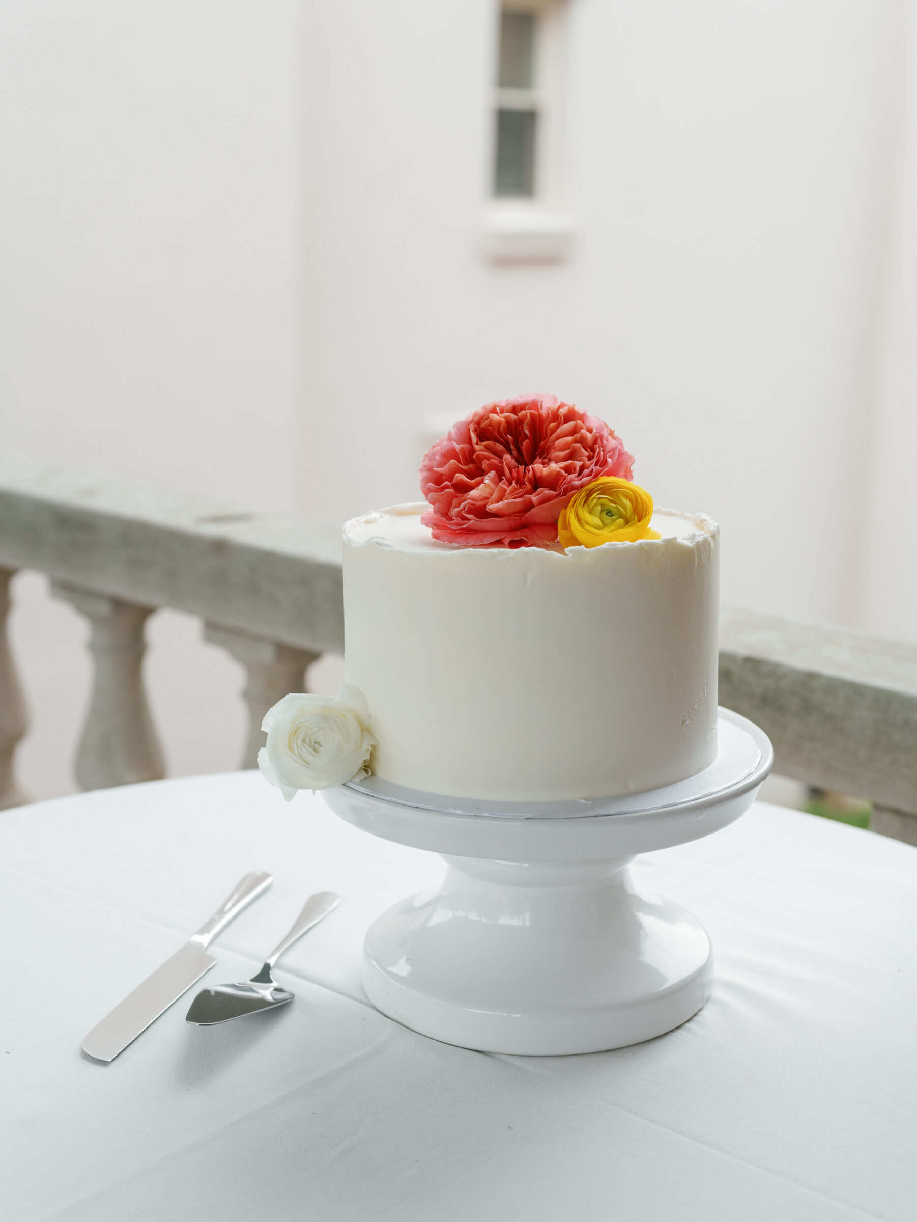 Elegant single-tier white wedding cake decorated with fresh coral, yellow, and white flowers at a wedding reception in Washington DC.
