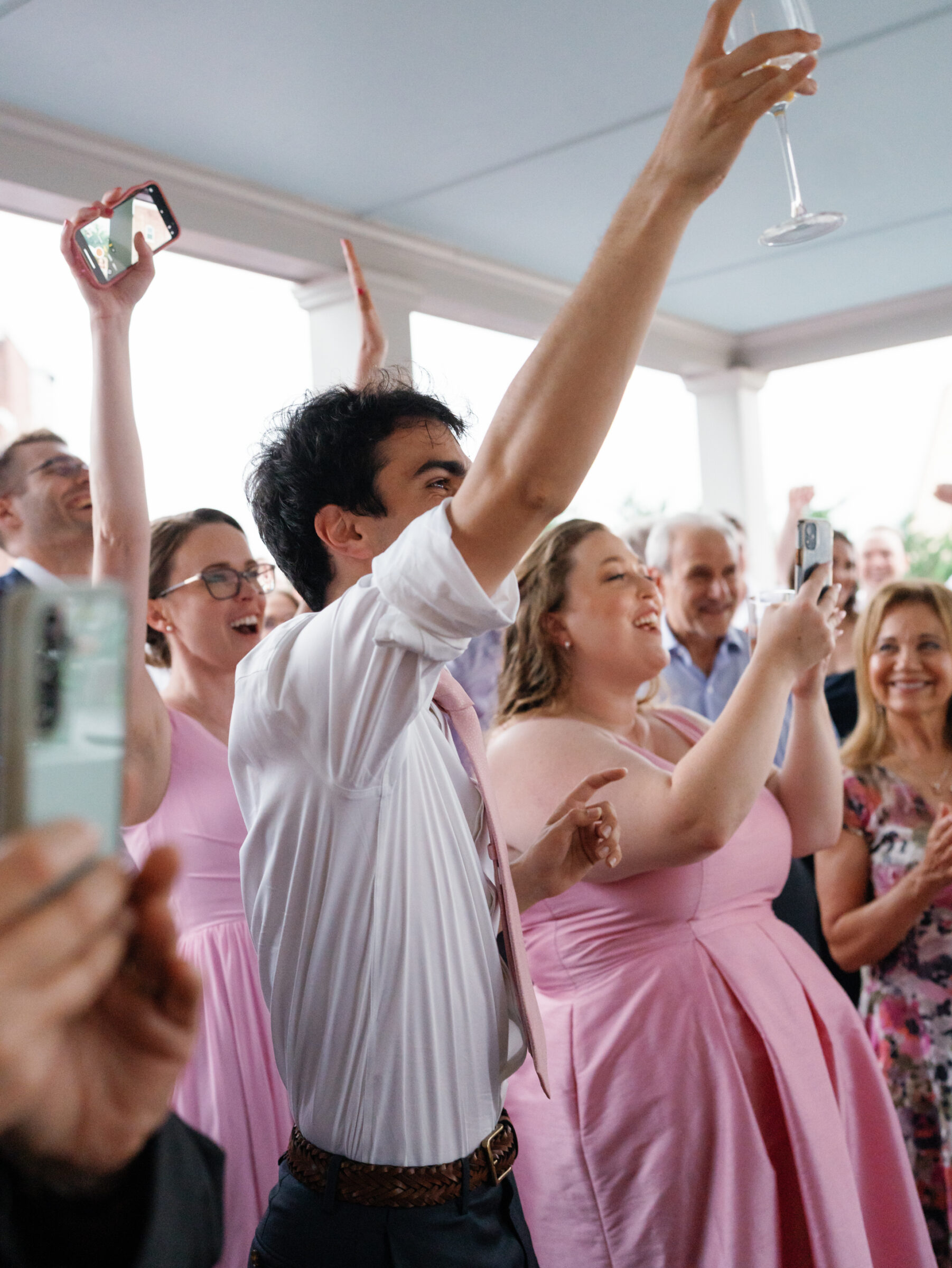 Wedding guests in pink bridesmaid dresses cheering and raising glasses during the reception at Woodrow Wilson House in Washington DC.