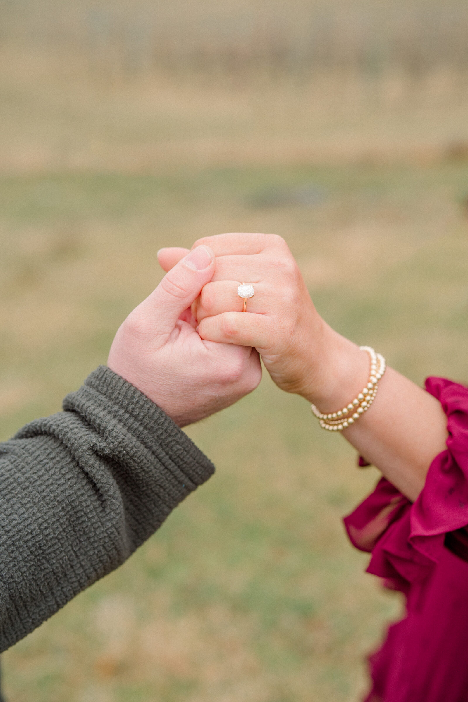 Close-up of a couple holding hands, featuring an oval engagement ring and pearl bracelet.