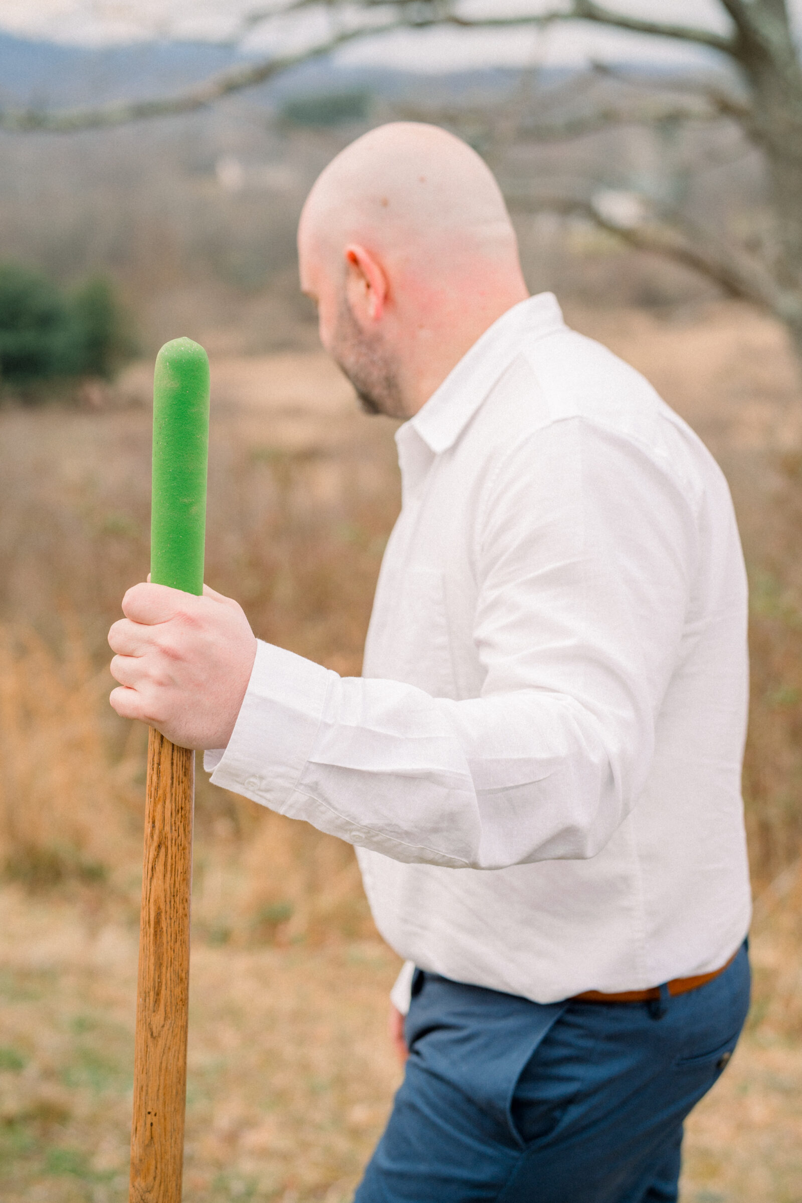 Groom-to-be holding a shovel during a bourbon burying ceremony with vineyard hills in the background.