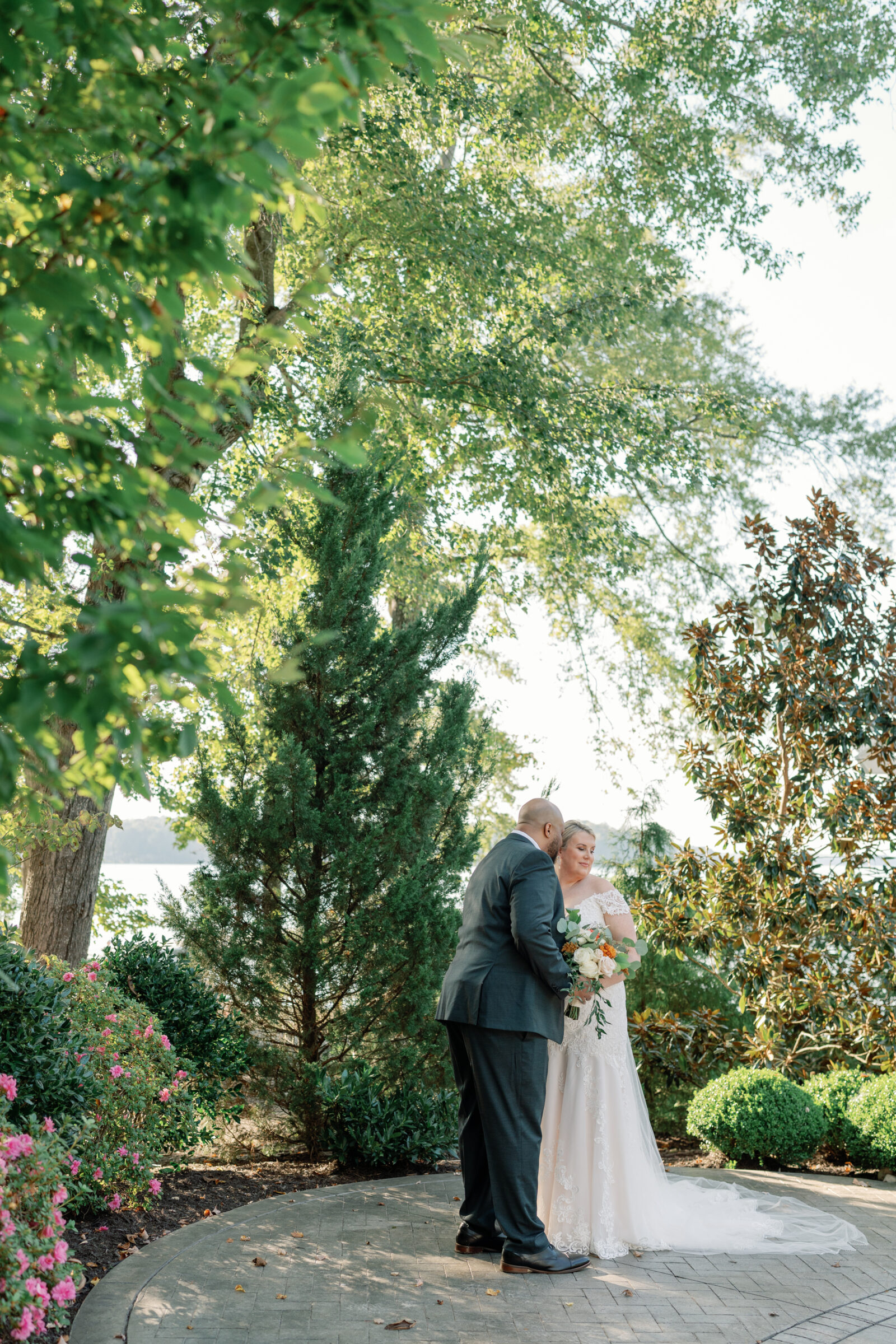 Bride and groom share a quiet moment during their wedding at The Boathouse at Sunday Park in Richmond VA, standing on a brick path surrounded by greenery and lake views.