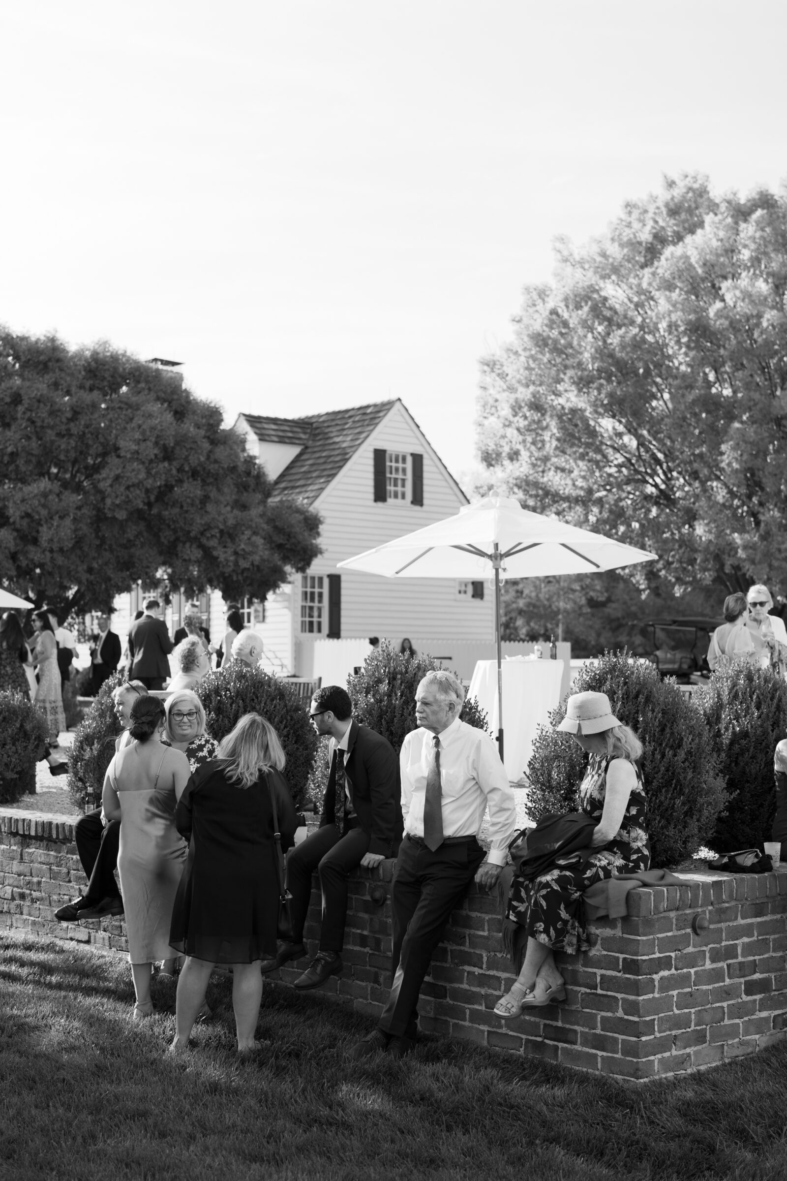Black and white photo of wedding guests mingling during cocktail hour outside the white manor house at Burlington Weddings & Events in Charles City VA.