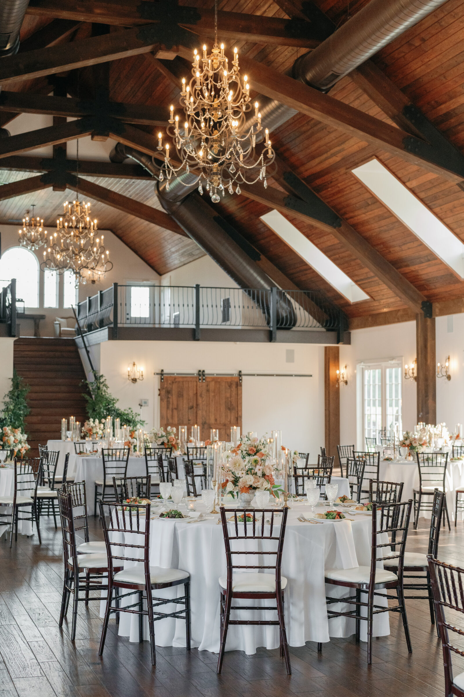 Elegant wedding reception setup with white linens, floral centerpieces, and chandeliers inside the grand ballroom at Burlington Weddings & Events in Charles City VA.