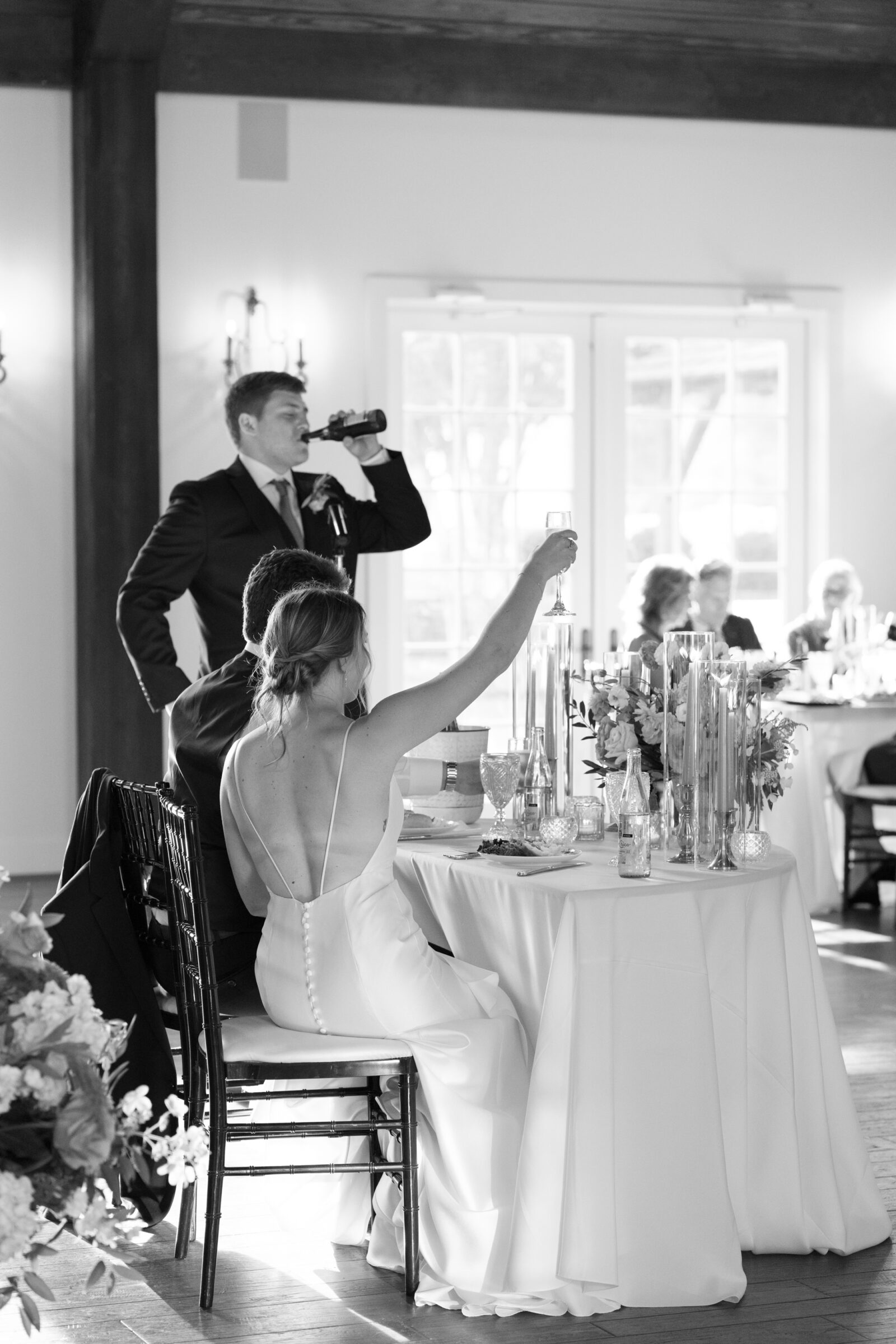 Black and white photo of bride raising a champagne glass during wedding toasts at Burlington Weddings & Events in Charles City VA.