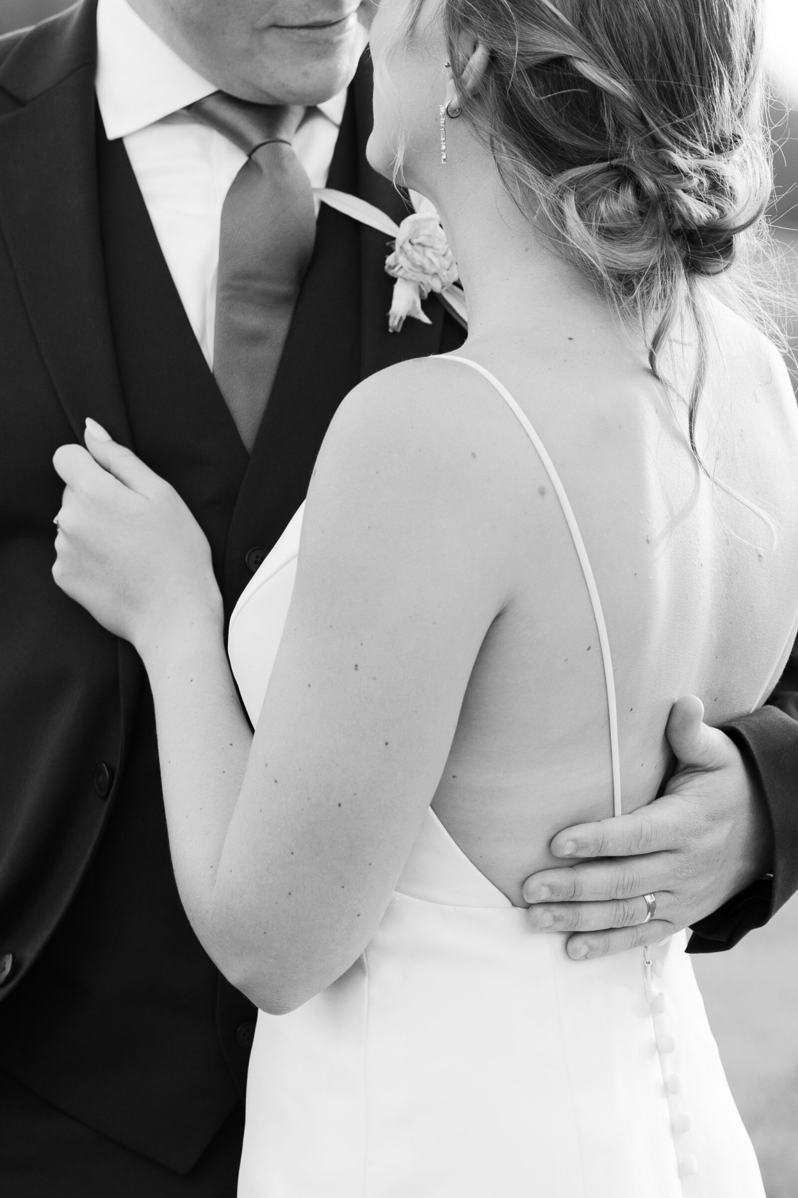 Black and white close-up of groom holding the bride’s back as they share a quiet moment during sunset portraits.