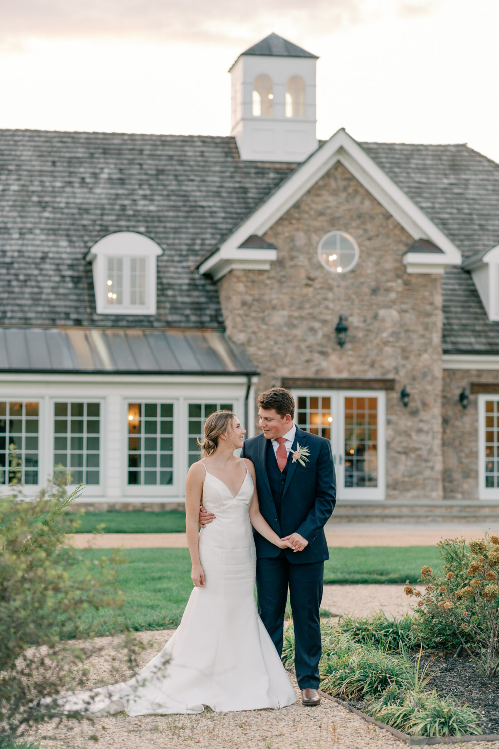 Bride and groom standing in front of the stone façade of Burlington Weddings & Events in Charles City VA during sunset portraits.