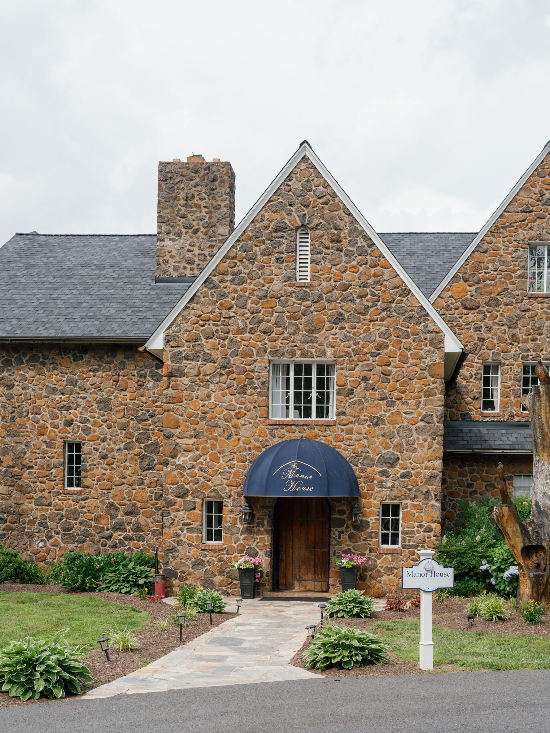 Exterior view of Poplar Springs Manor in Warrenton VA with stone façade, blue awning, and landscaped entrance, perfect for a Poplar Springs Manor wedding.