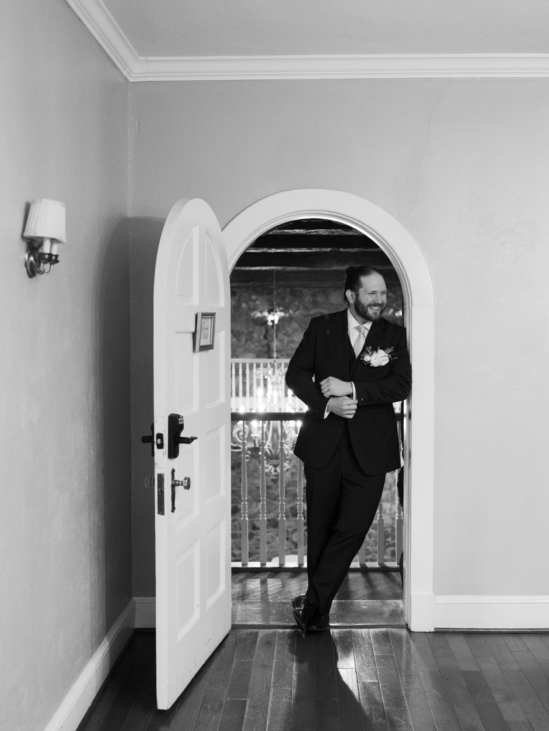 Black and white portrait of the groom smiling and leaning in a doorway inside the manor house during a Poplar Springs Manor wedding in Warrenton VA.