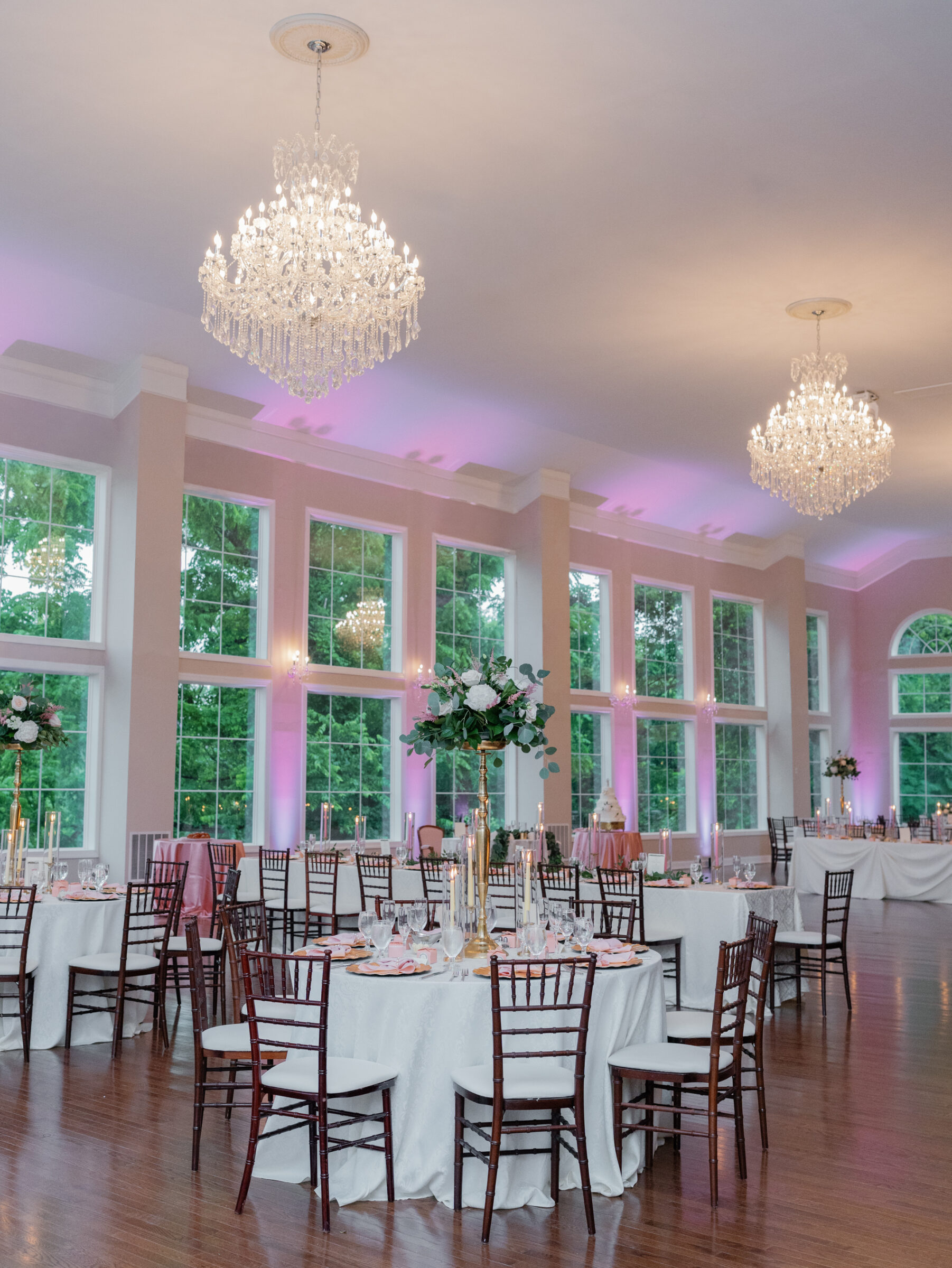 Reception ballroom at Poplar Springs Manor wedding in Warrenton VA with tall floral centerpieces, chandeliers, and pink uplighting against large windows.