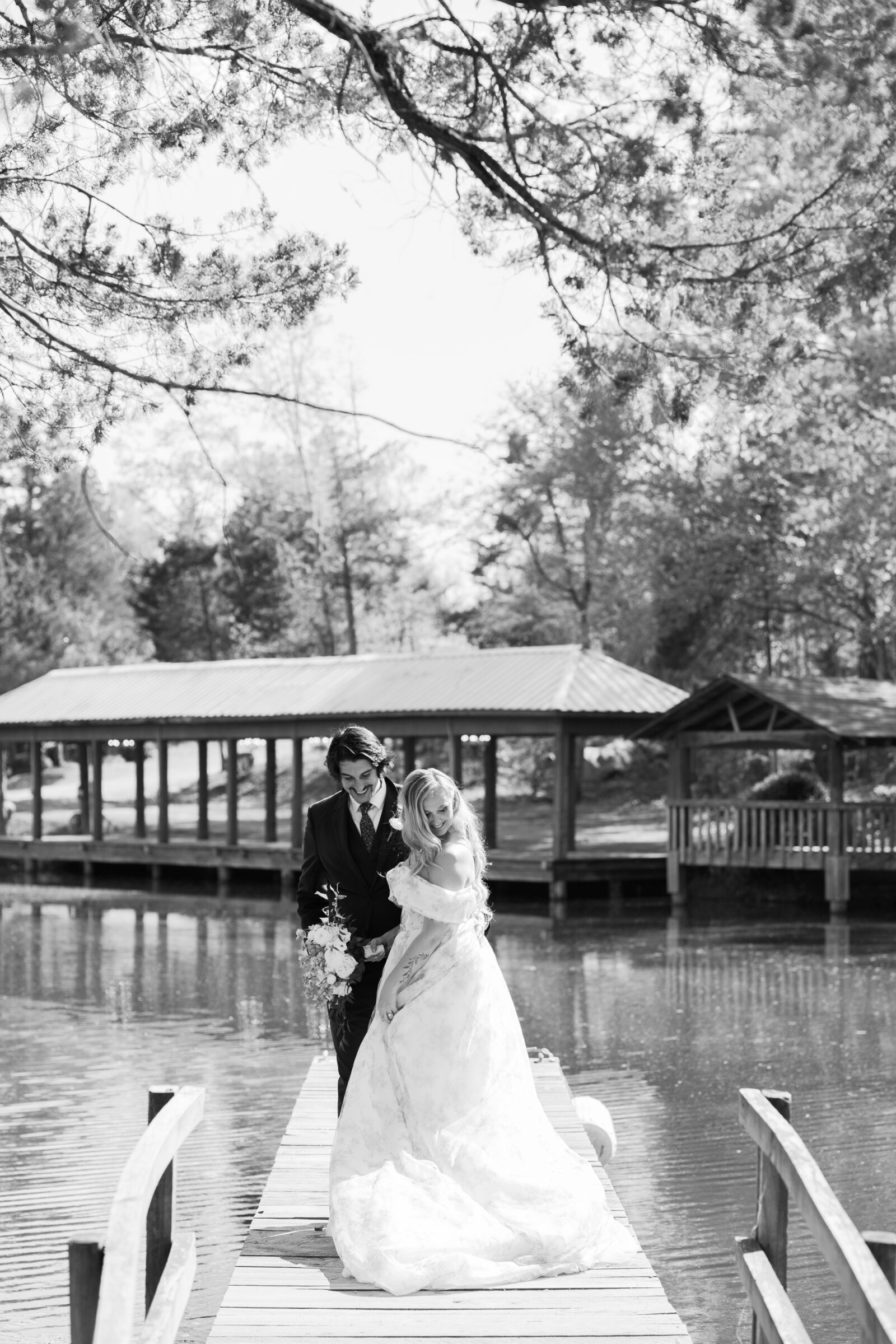 Bride and groom walk together across a wooden dock over the water at Rassawek Vineyards in Virginia, captured in timeless black and white during their vineyard wedding.
