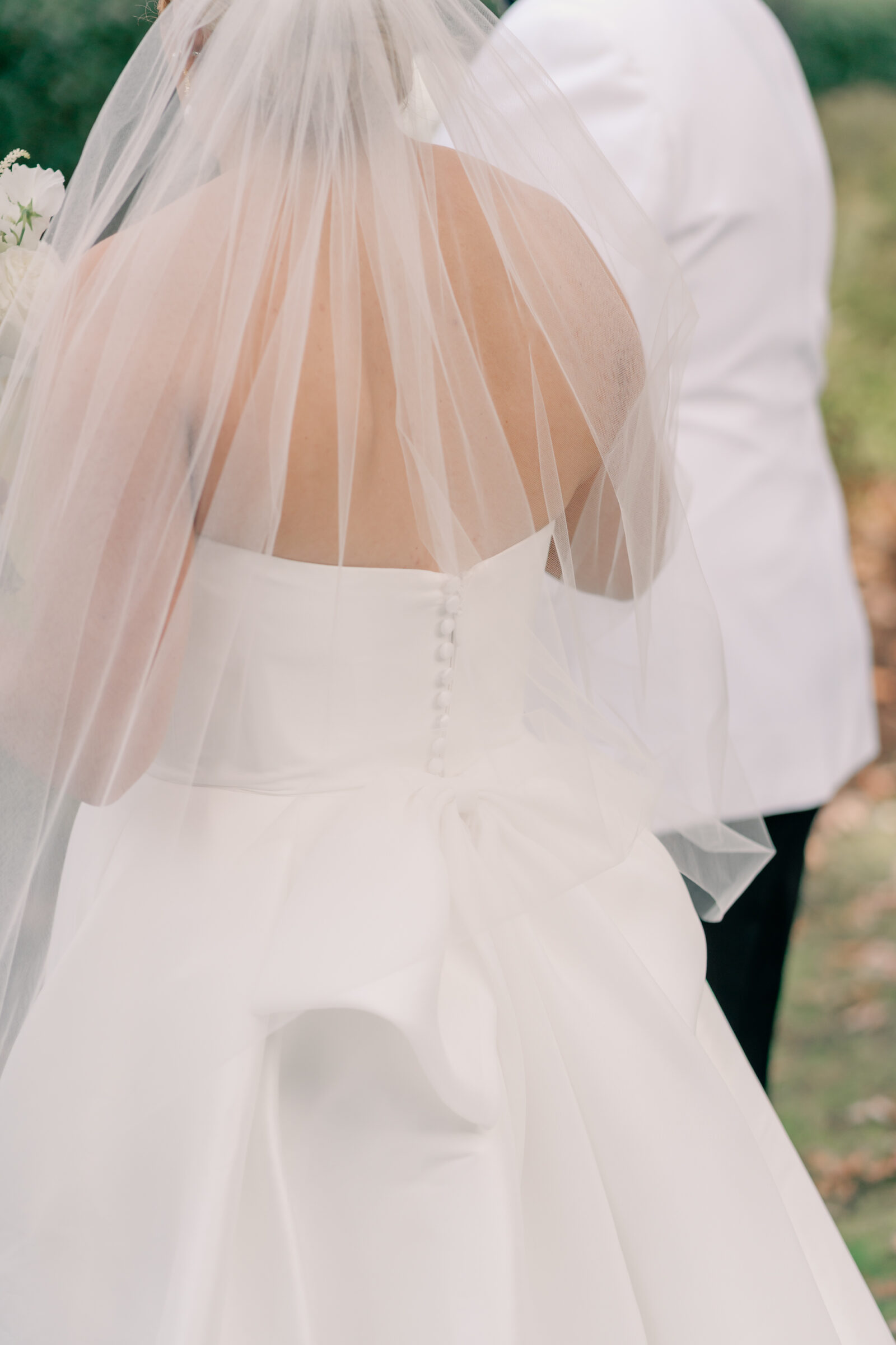 Close-up of the bride’s wedding gown and veil, highlighting the button detail and large bow on the back of the dress.