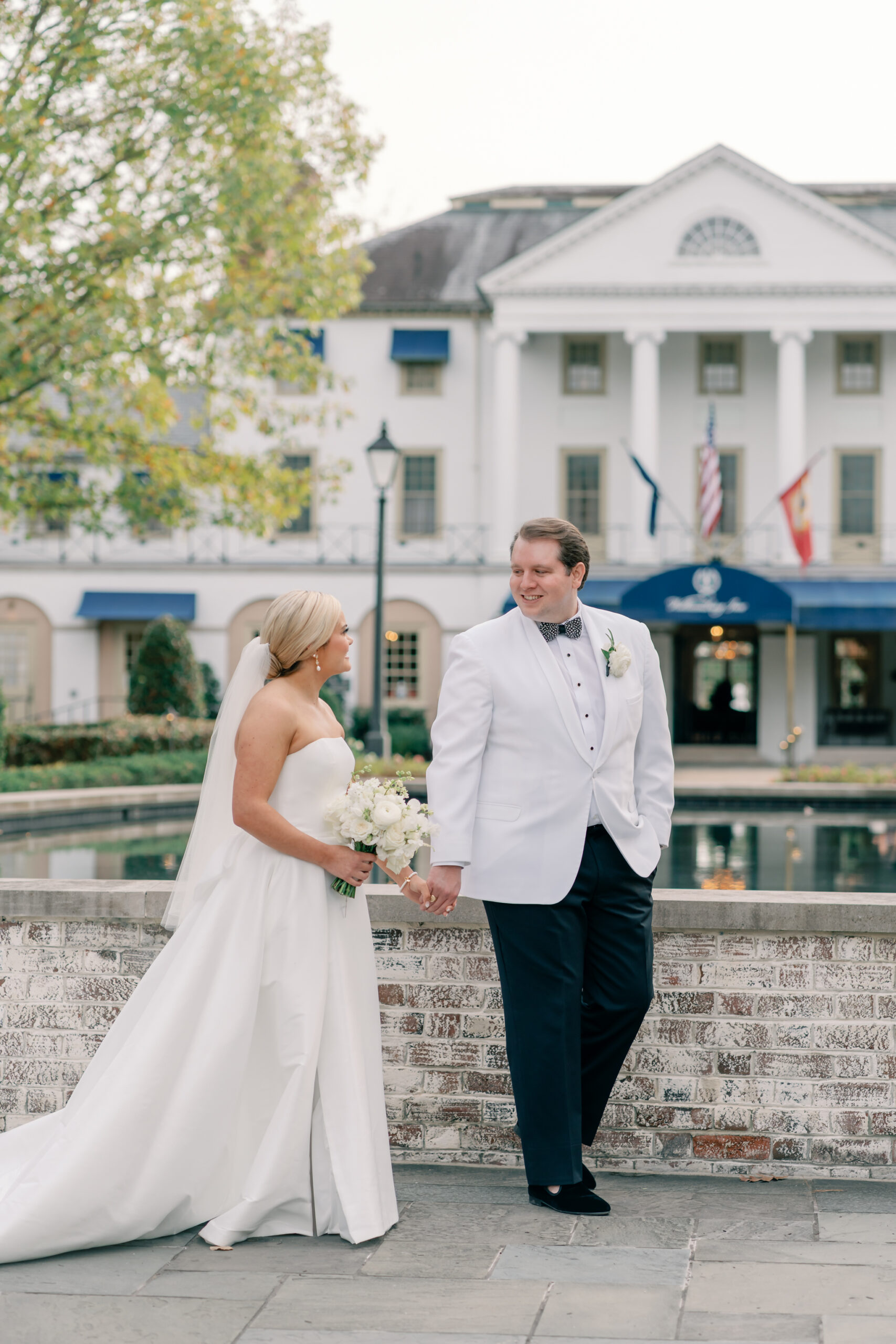 Bride and groom holding hands by the fountain at the Williamsburg Inn wedding venue, with the historic white façade and columns in the background.