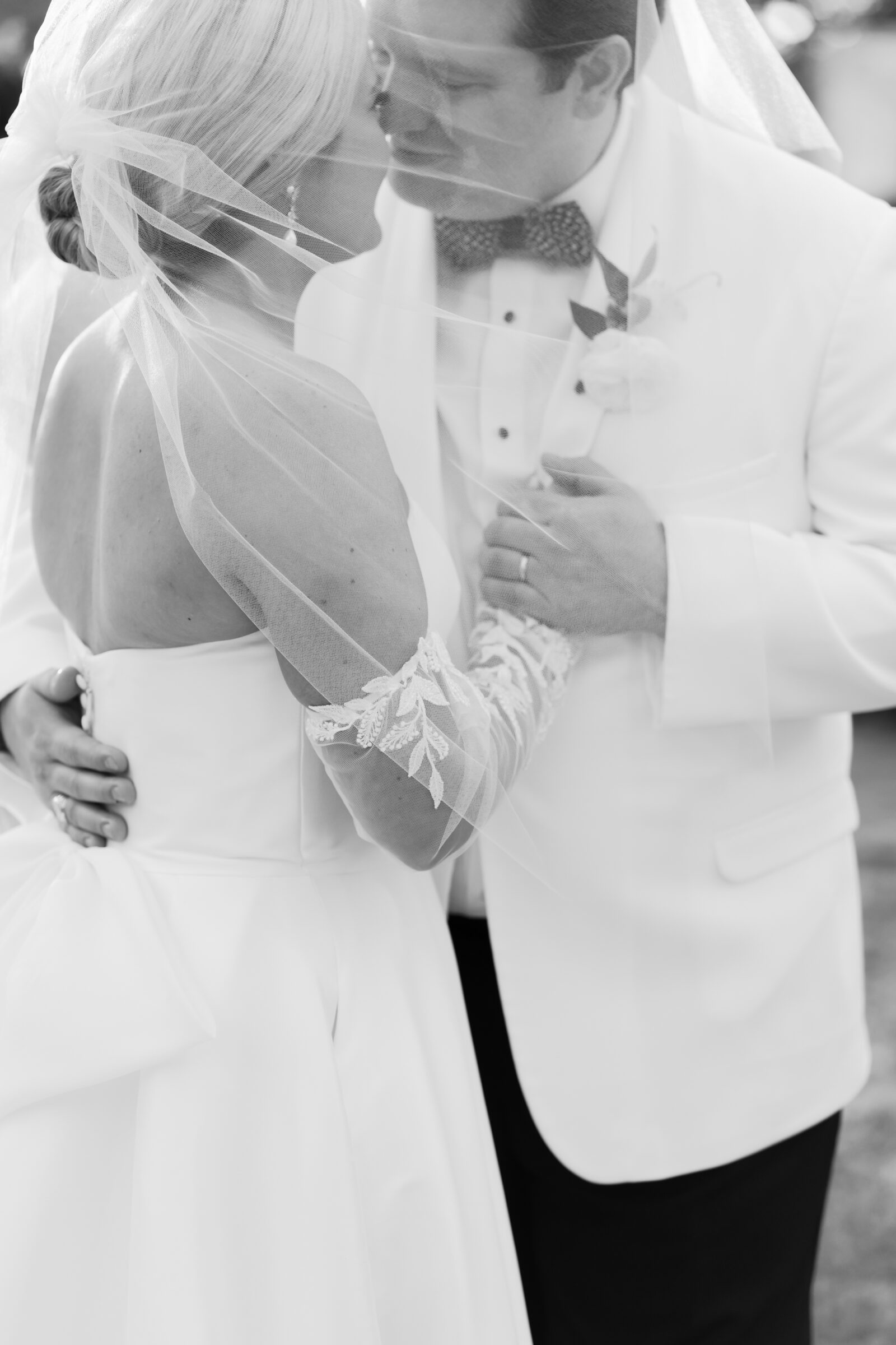 Romantic black and white photo of the bride and groom under her veil, sharing a quiet embrace.