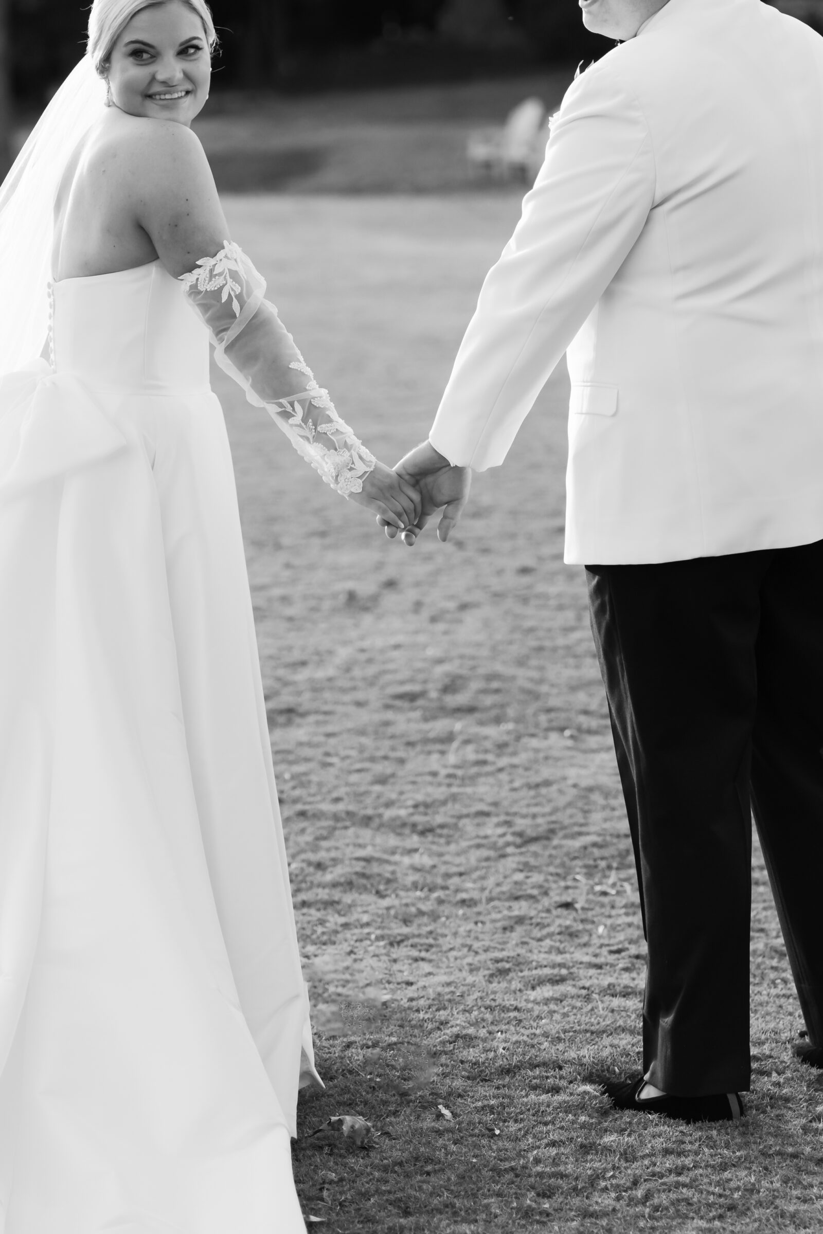 Black and white photo of the bride smiling back at the camera while holding hands with the groom during their Williamsburg Inn wedding.