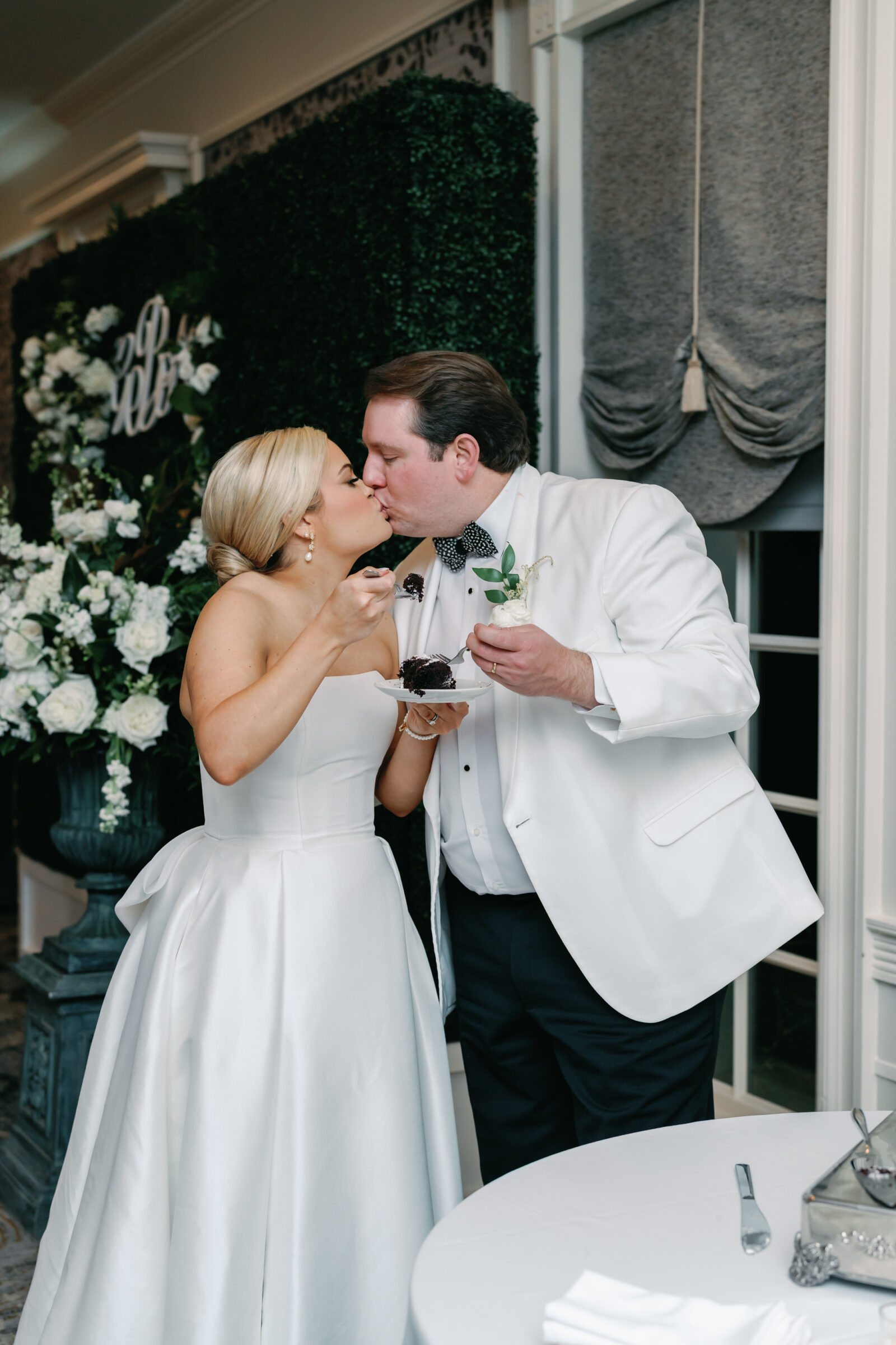 Bride and groom share a kiss while cutting and enjoying cake during their Williamsburg Inn wedding reception.