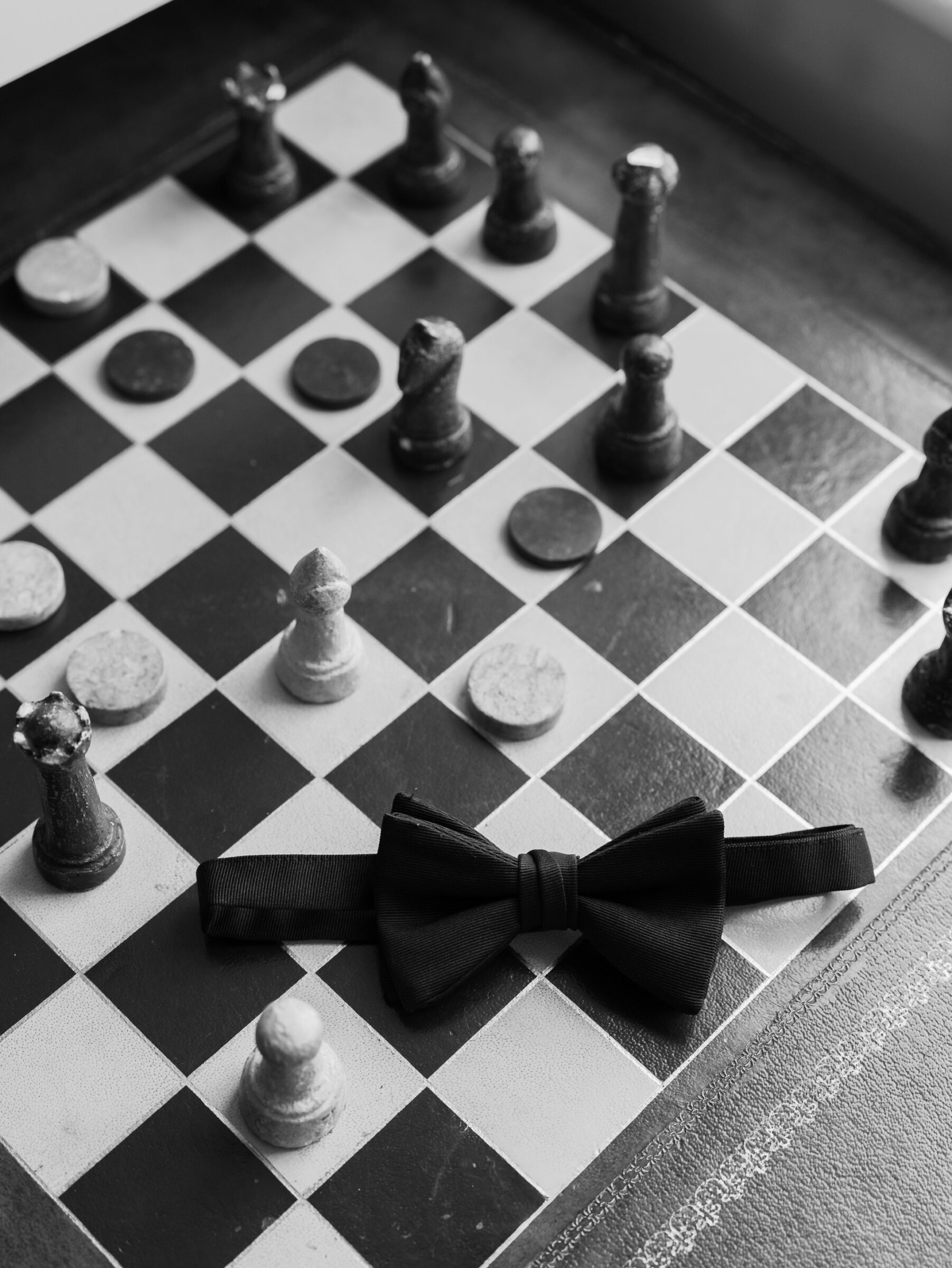 Black bow tie resting on a vintage chessboard with wooden chess pieces