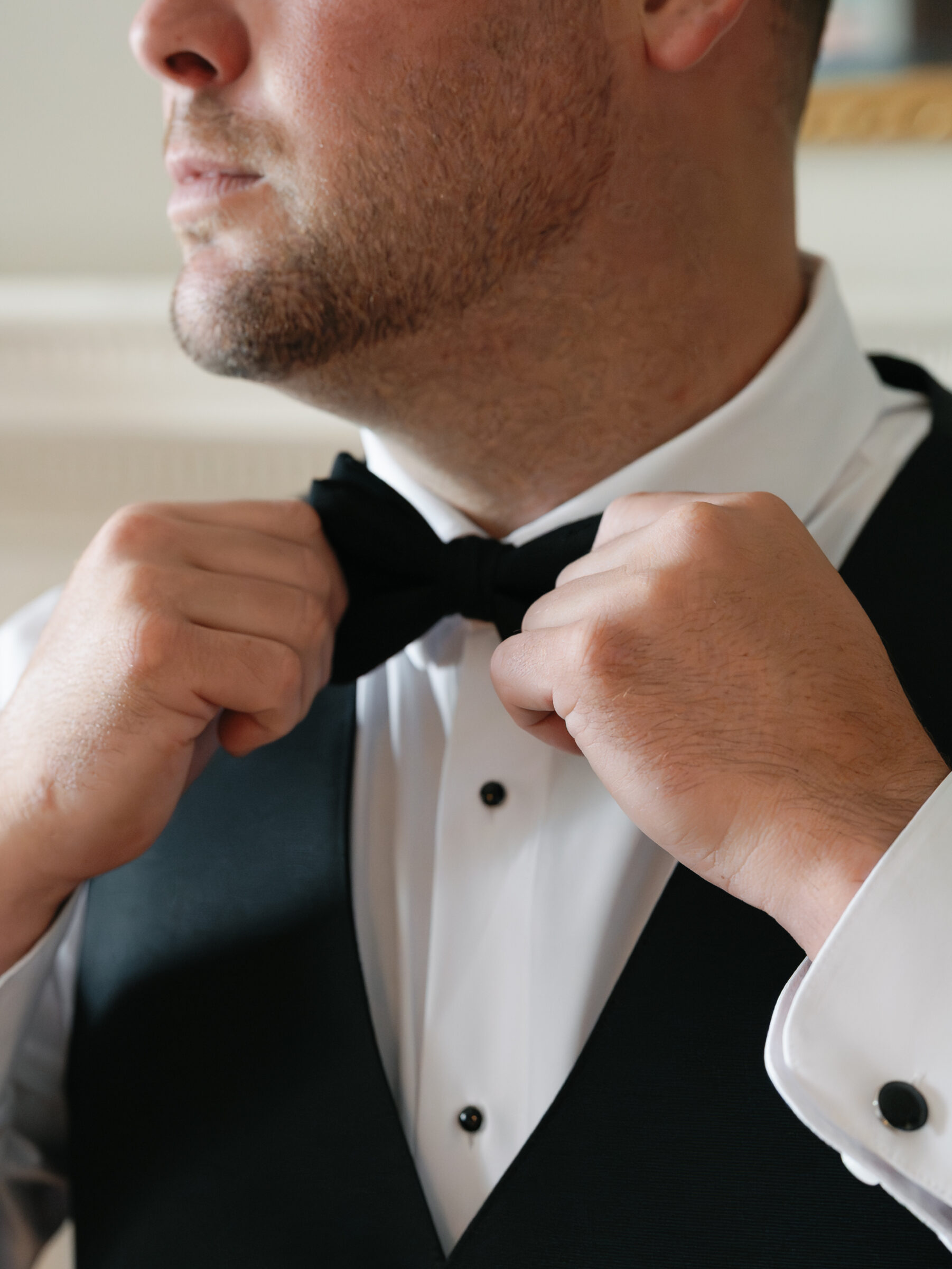 Groom adjusting his black bow tie while getting ready for a wedding at Belmont Country Club in Ashburn, VA.