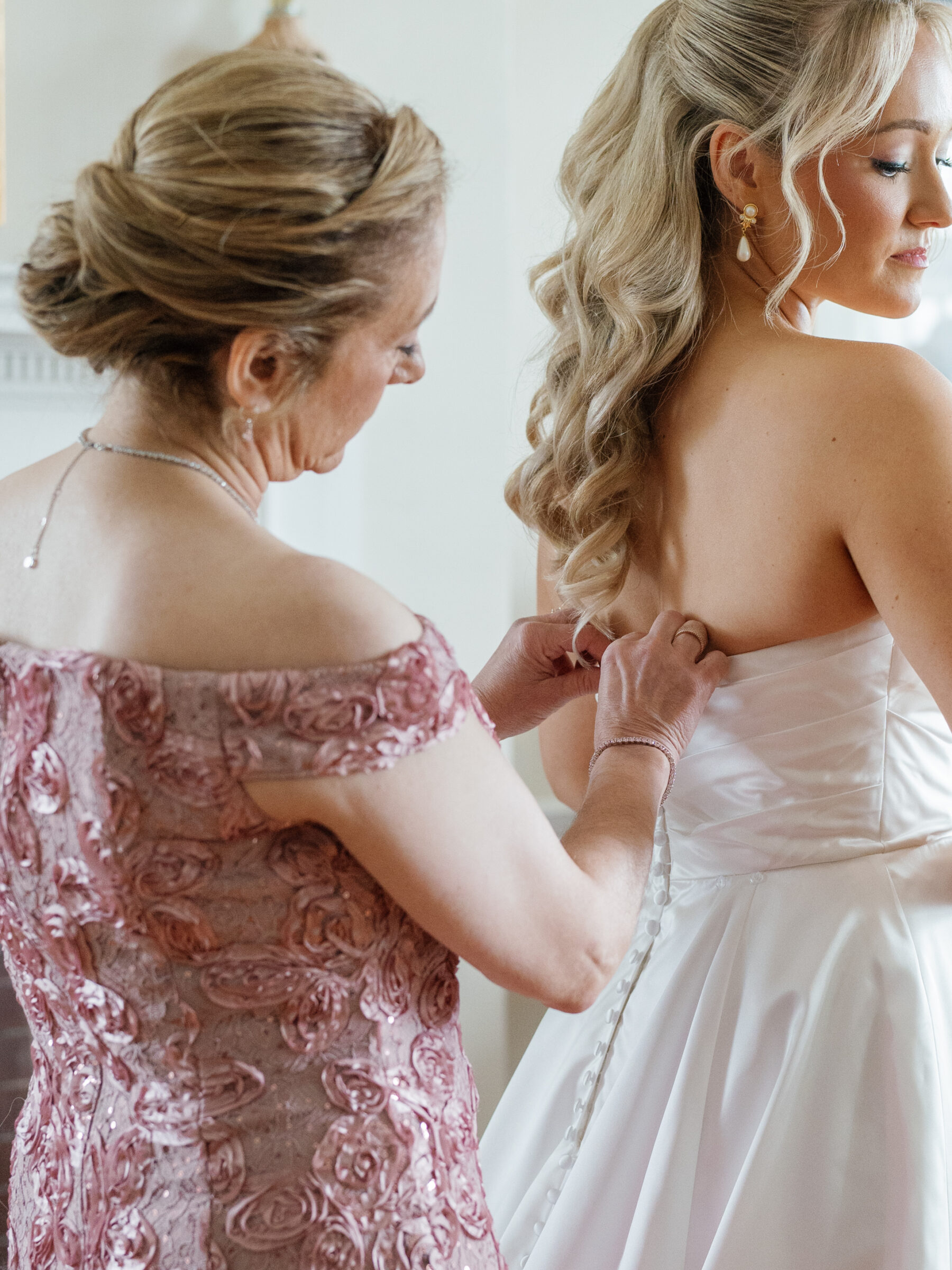 Mother helping bride button her wedding gown