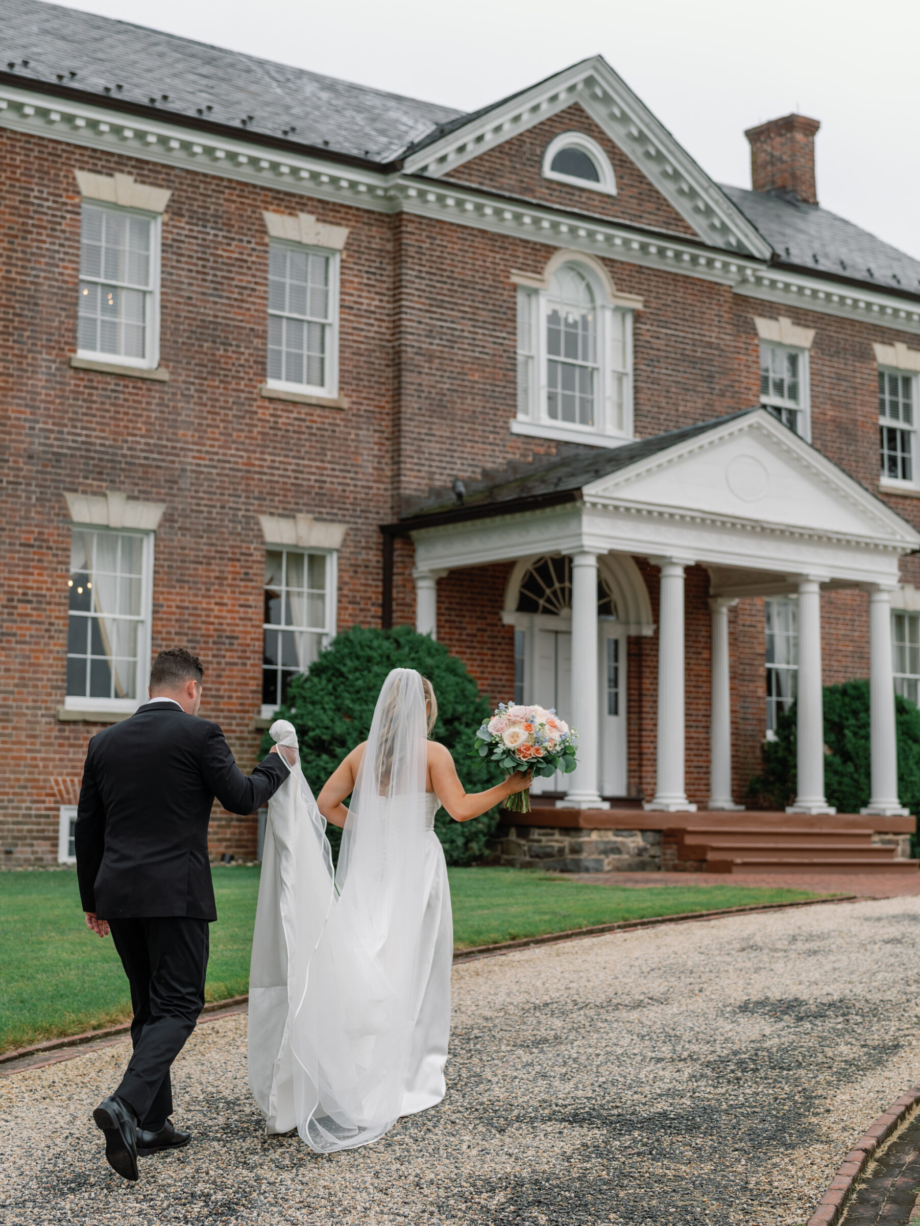 Bride and groom walking hand in hand toward the historic manor house at Belmont Country Club in Ashburn, VA.