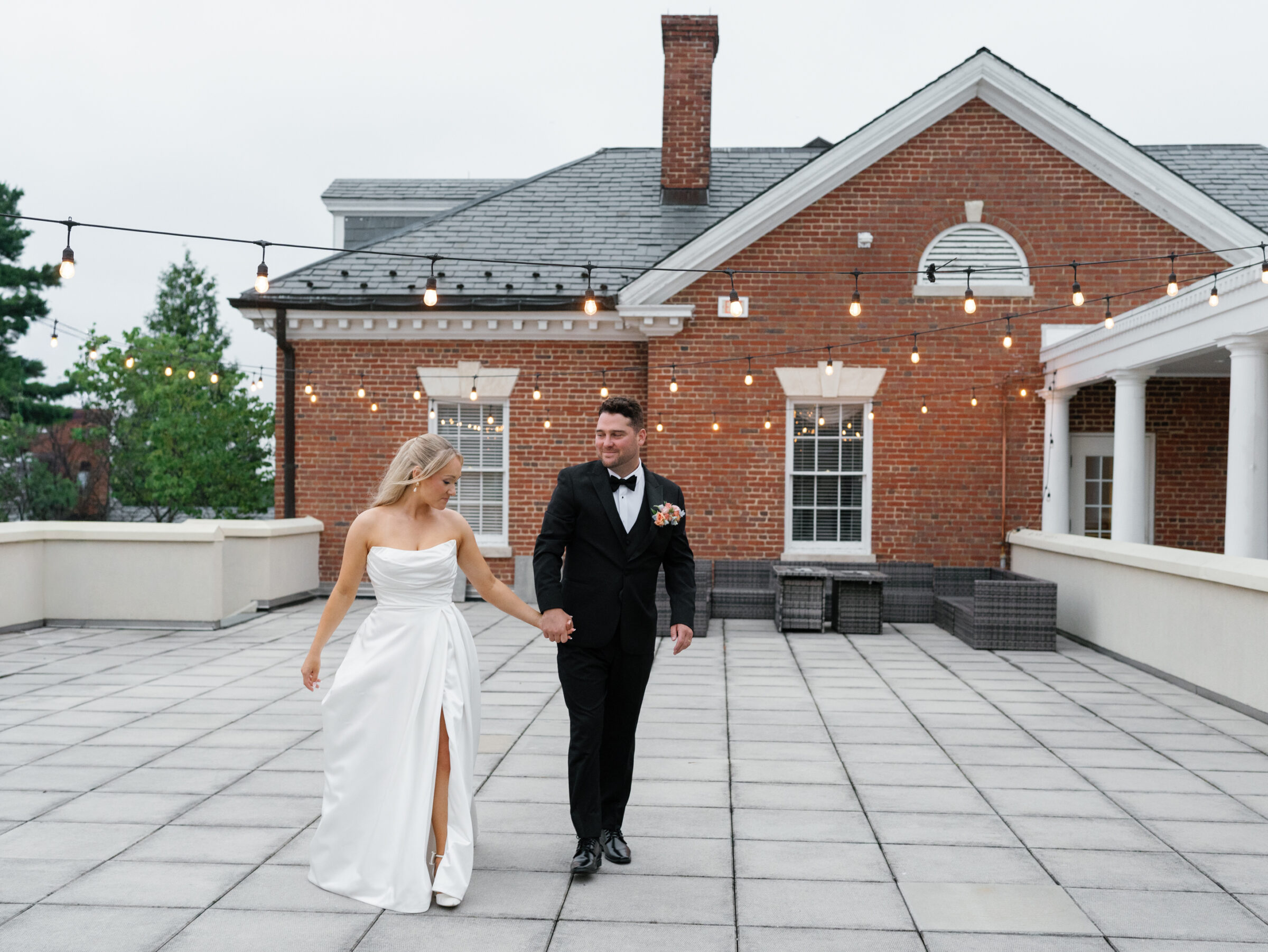 Bride and groom holding hands on the terrace with string lights at Belmont Country Club in Ashburn, VA.